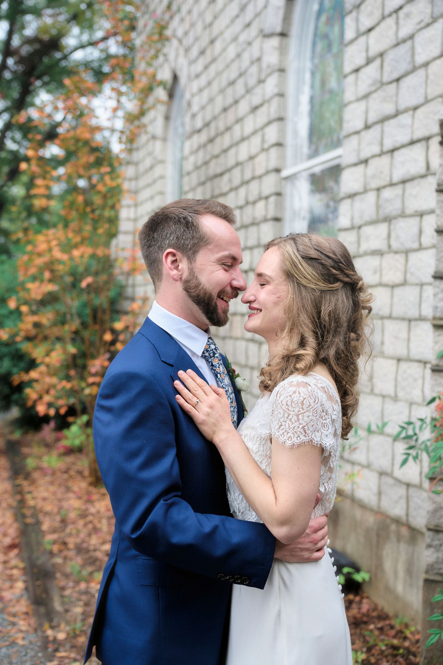 Candid wedding moment between a couple in formal attire sharing a loving glance against stone architecture.