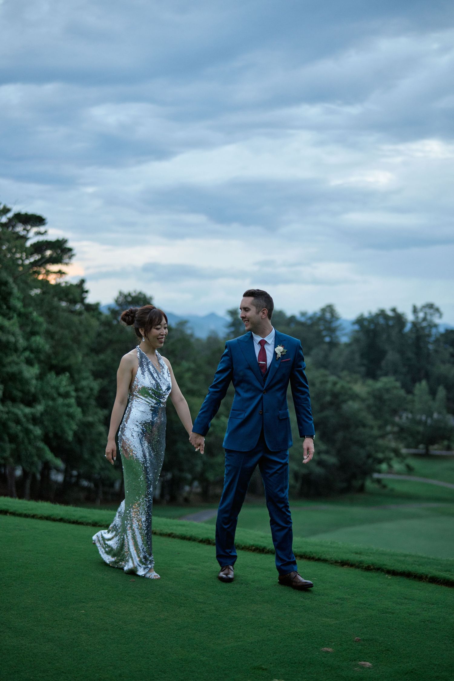 A couple in formal attire walks together on a misty golf course at twilight.