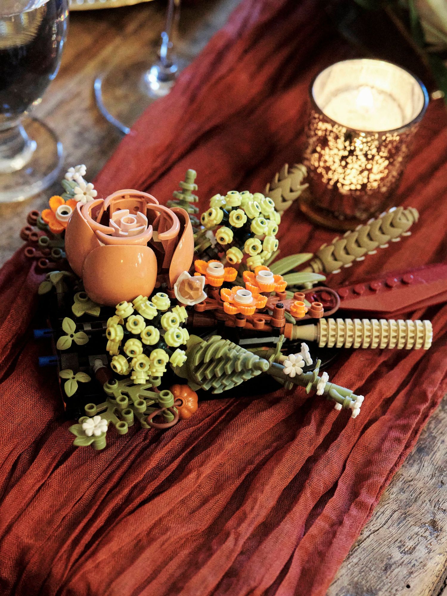Rustic floral arrangement with roses and greenery on burgundy fabric with glowing candle.