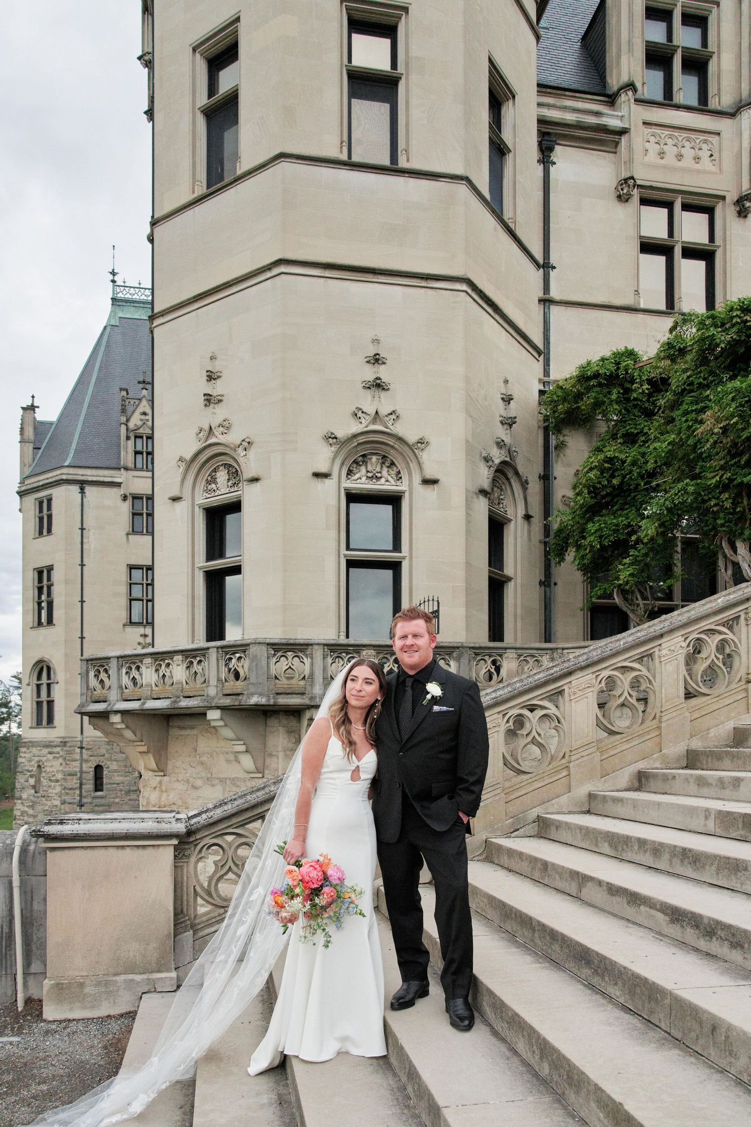 A couple poses on ornate stone steps of a historic building during their wedding ceremony.