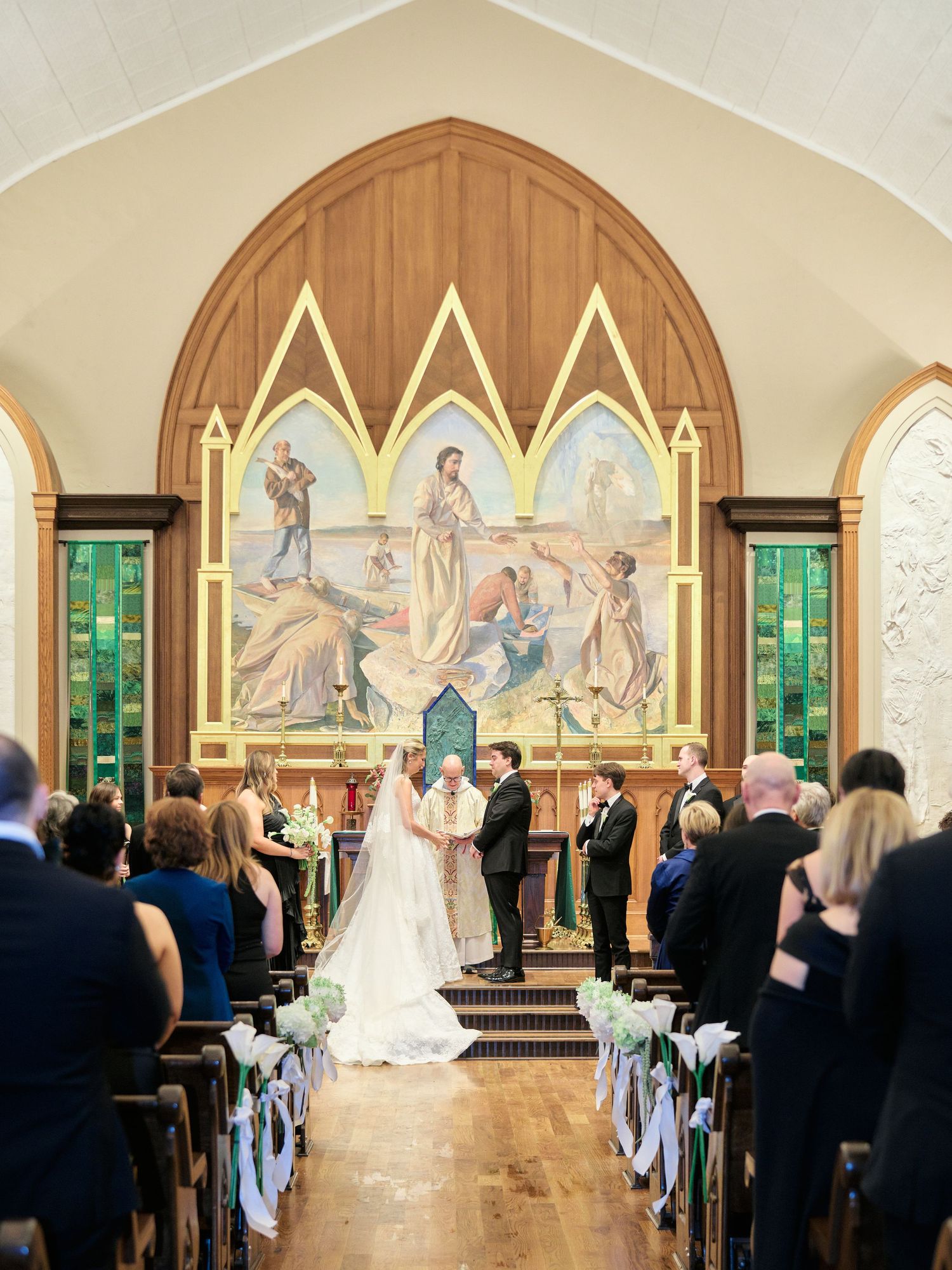 Bride and groom exchange vows at a church altar with stained glass windows and religious murals.
