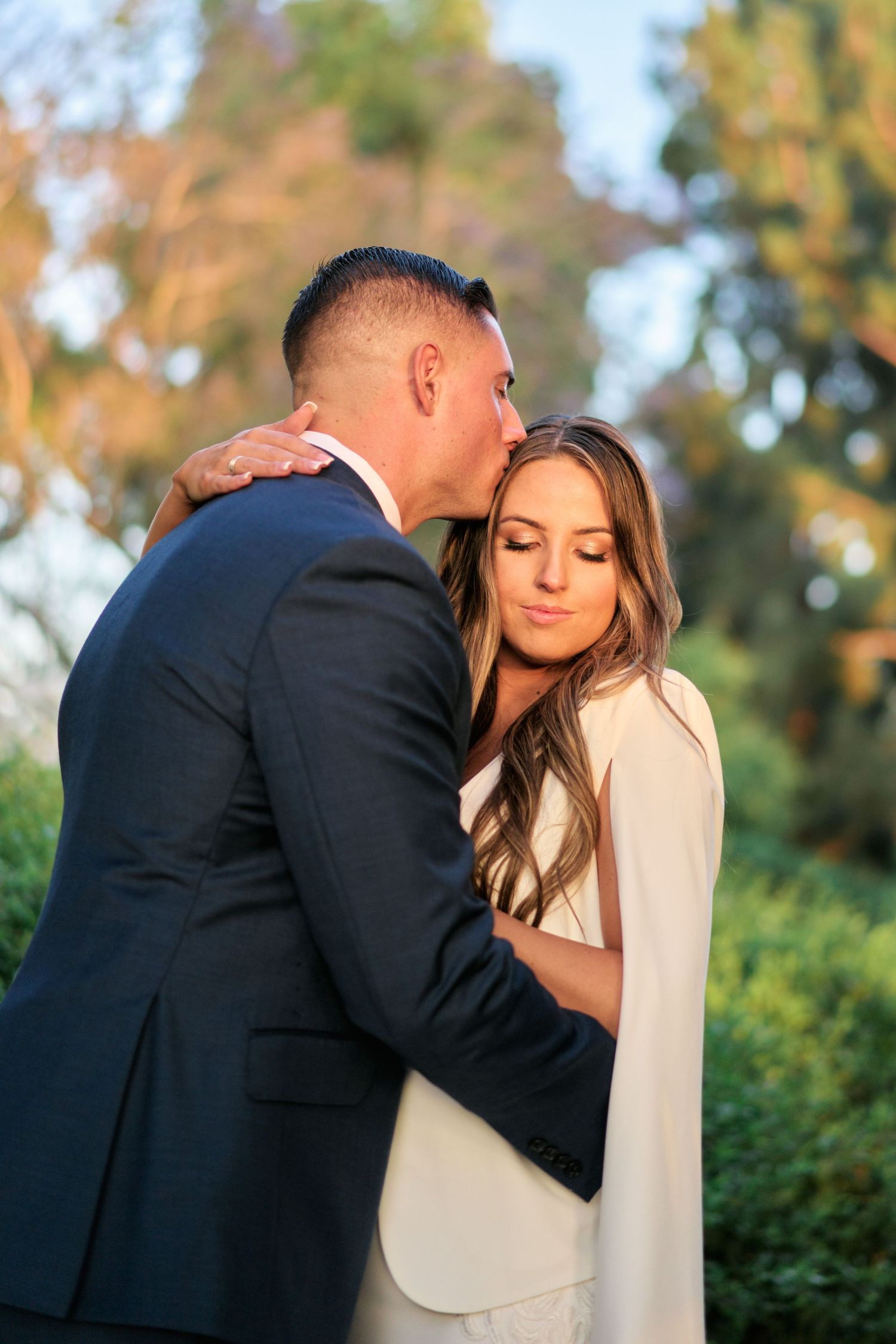 A romantic moment between a couple in formalwear captured during golden hour in a garden setting.