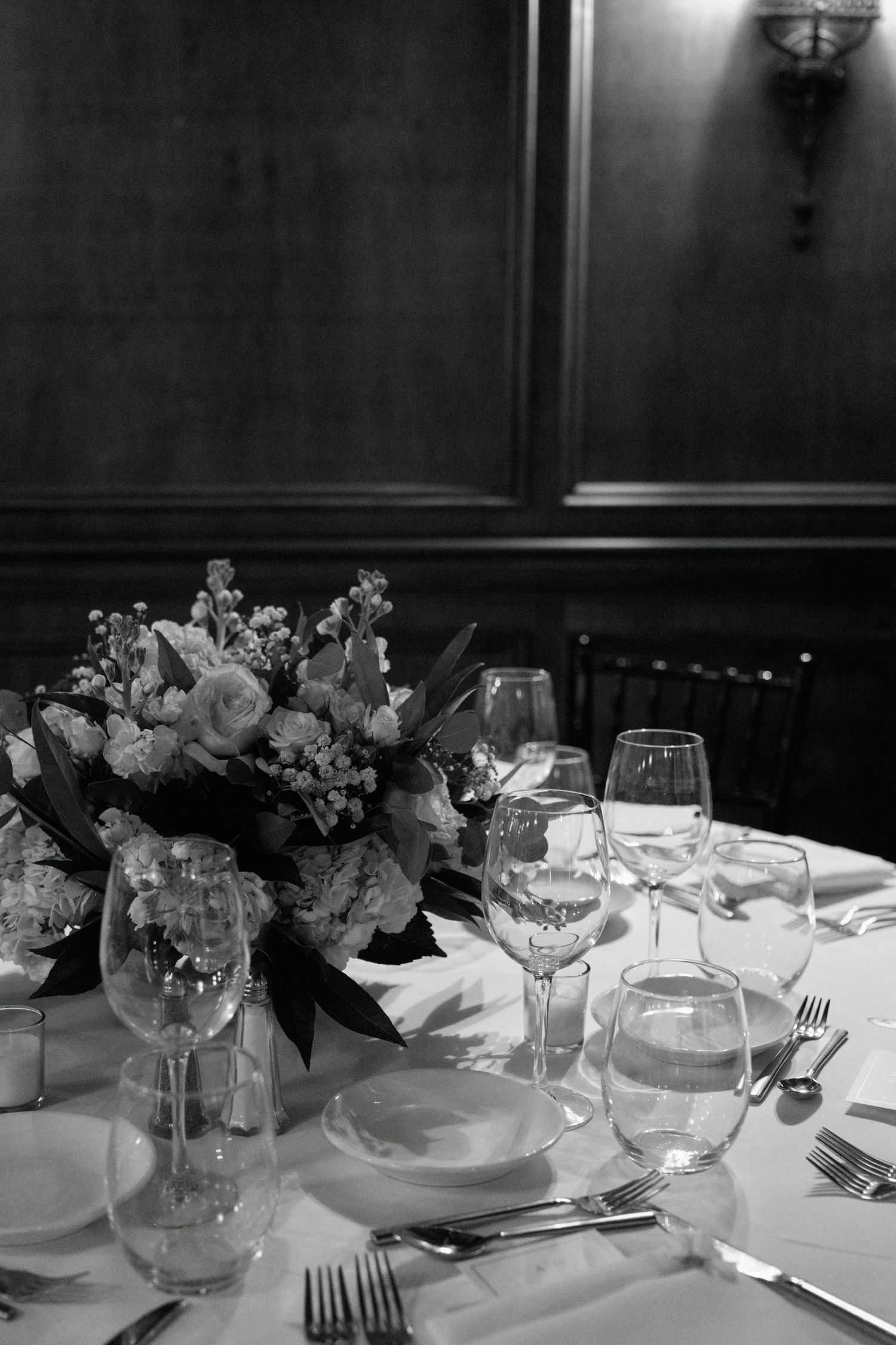 Elegant table setting with wine glasses and floral centerpiece in black and white photography.