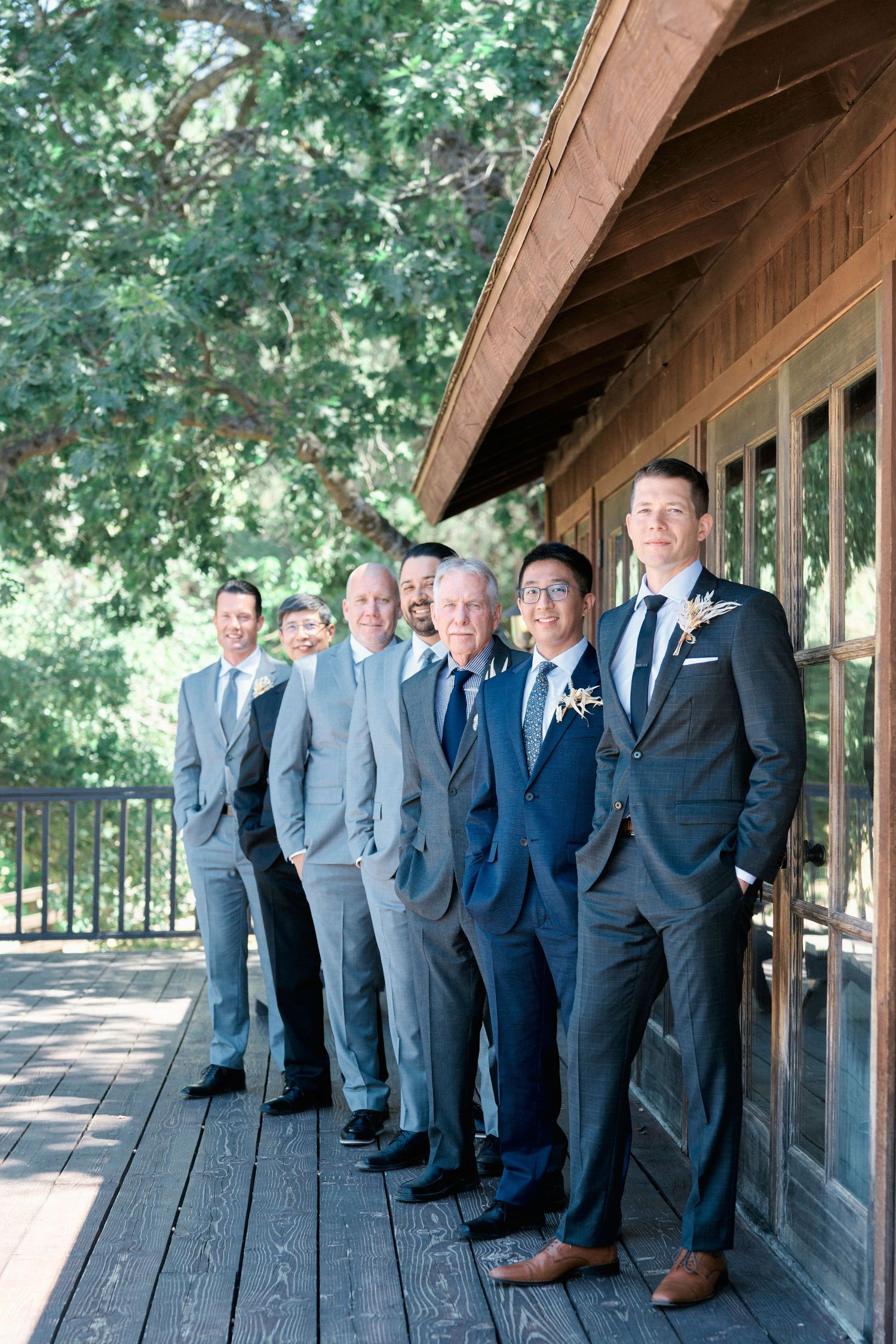 Wedding party members in coordinated suits pose on a rustic wooden deck.
