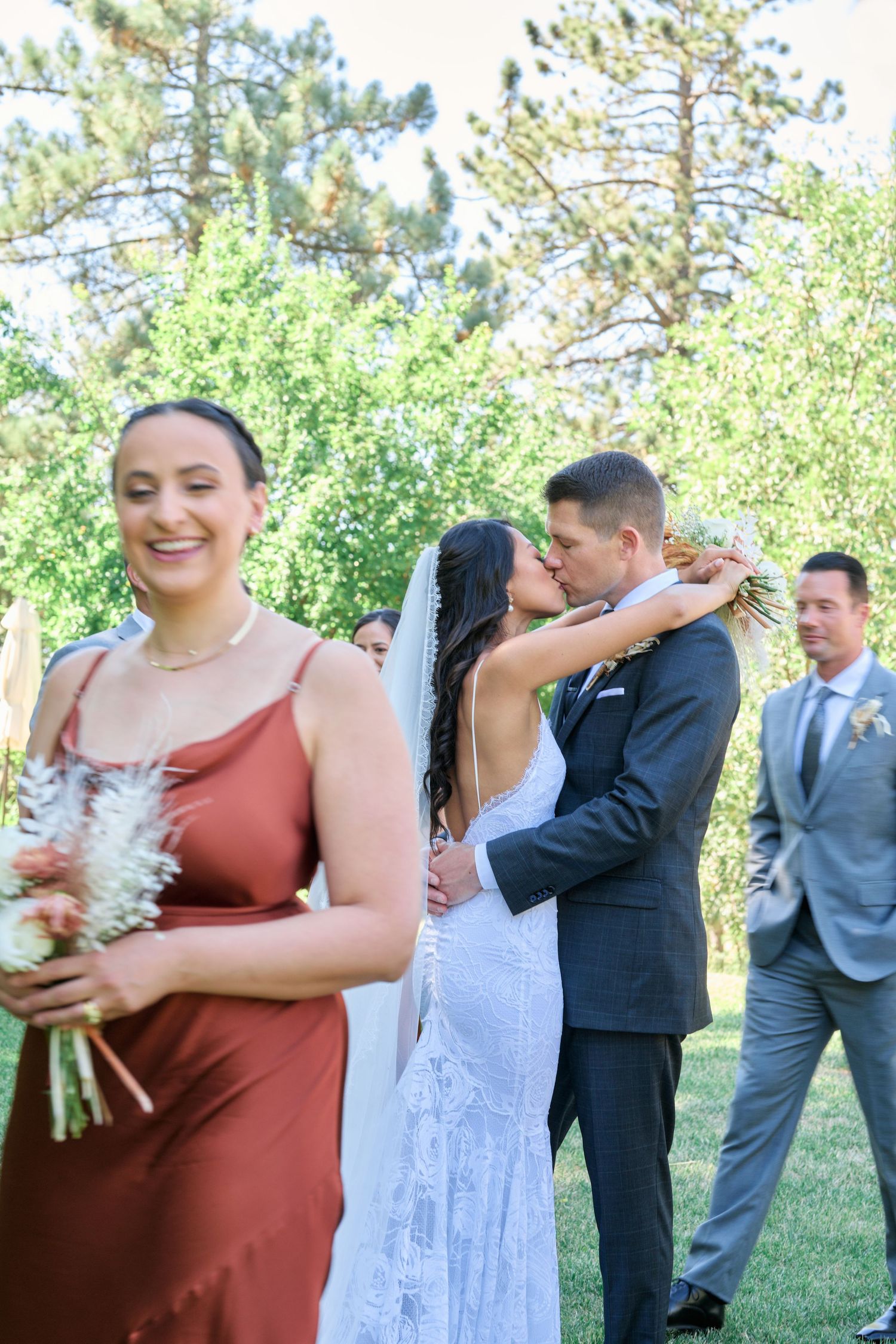 An outdoor wedding scene with bridal party members and bridesmaids in rust-colored dresses.