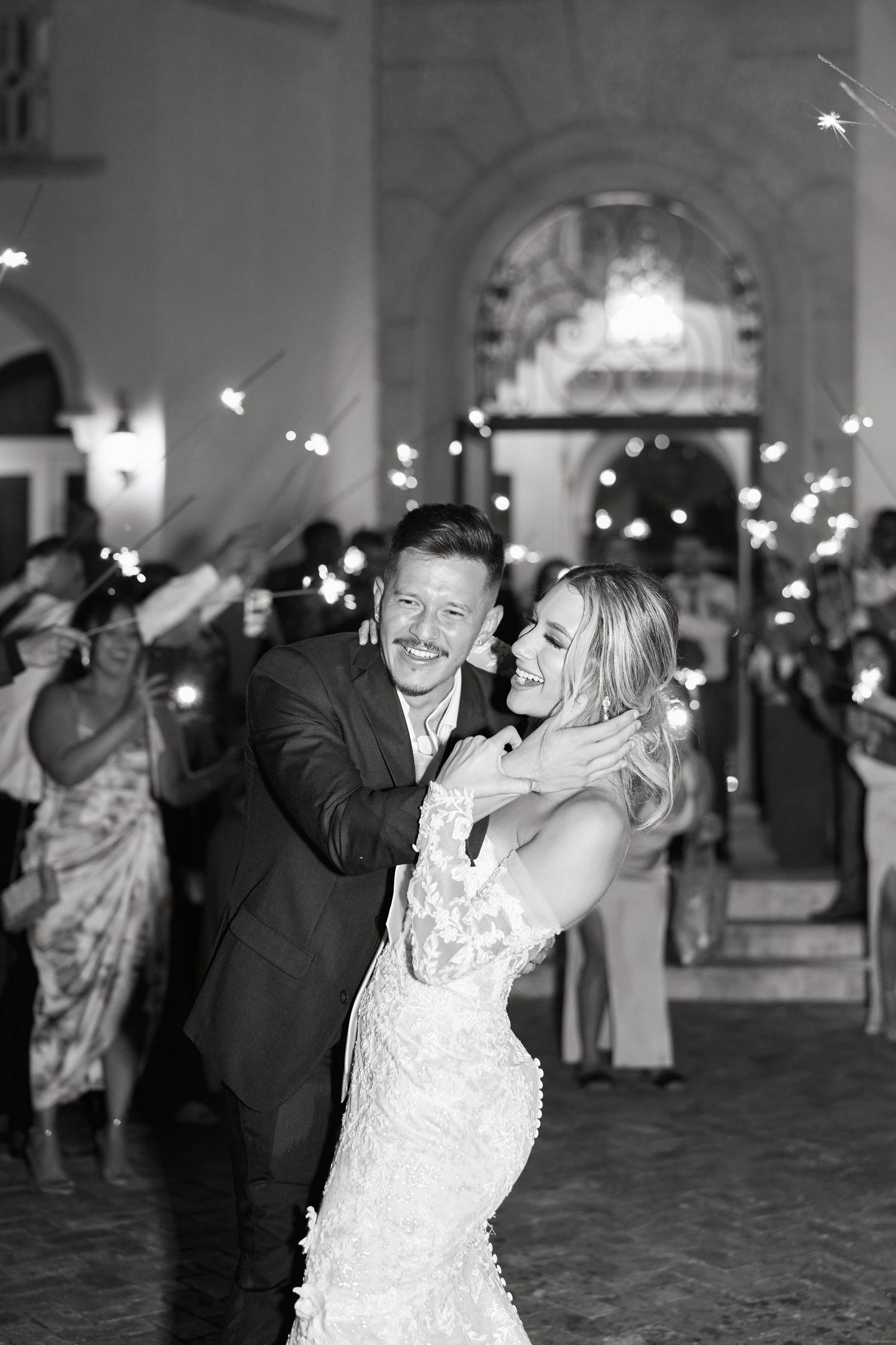 Black and white photo of newlyweds dancing amid sparklers at evening reception.