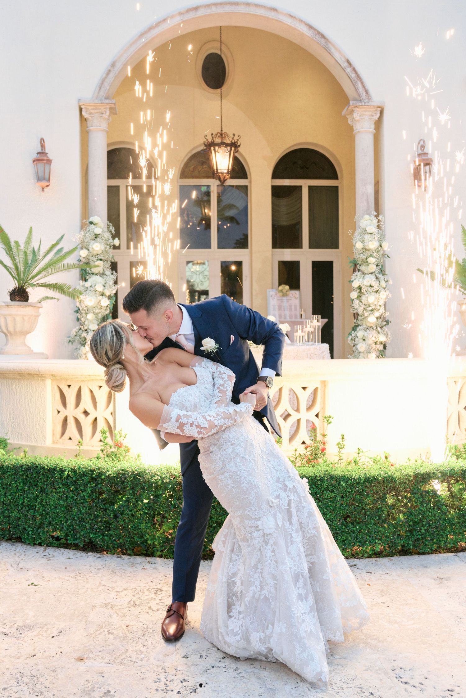 A romantic wedding dip pose in front of an elegant archway with white floral decorations and lanterns.