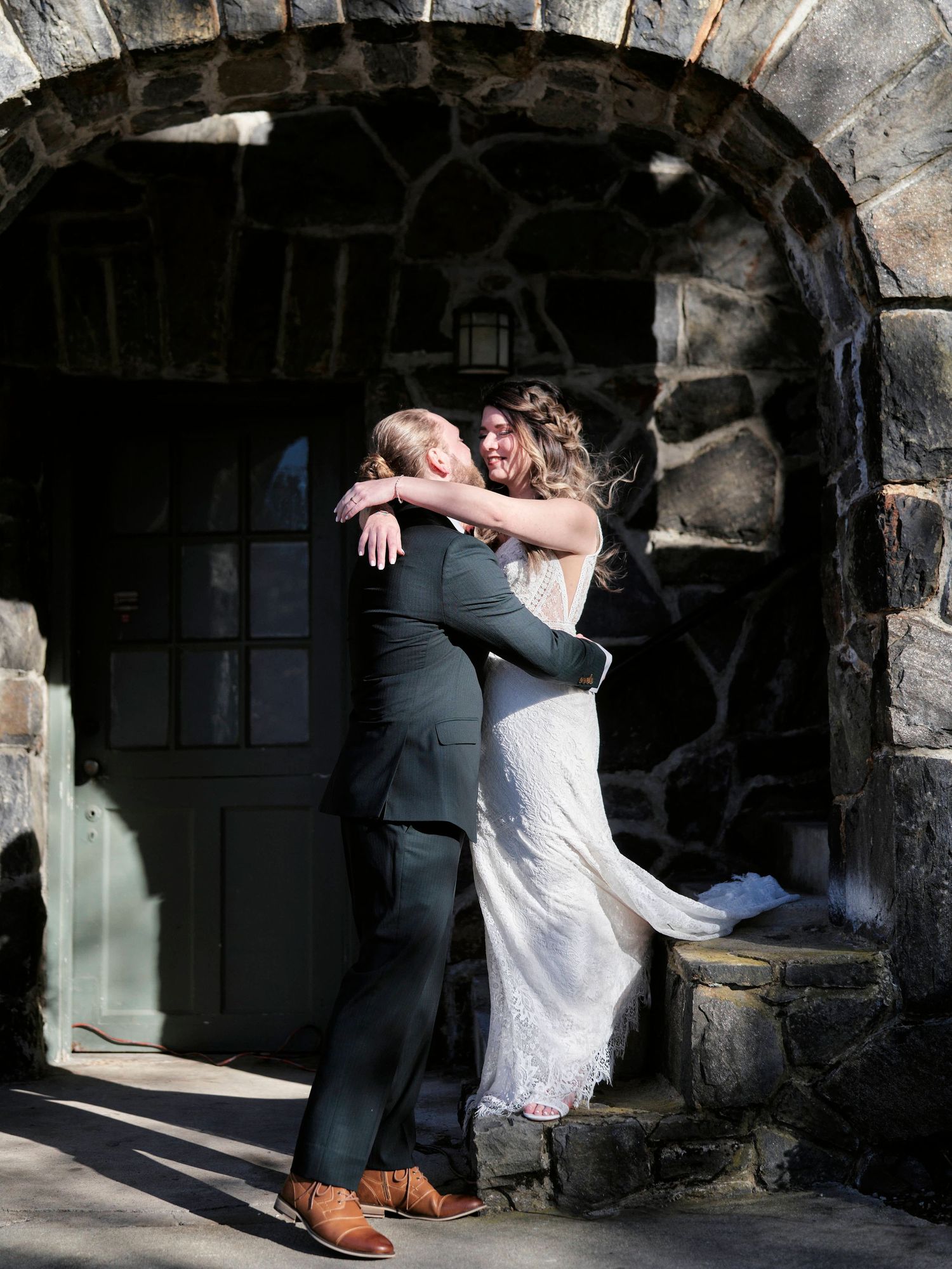 Newlyweds embrace under stone archway during romantic wedding portrait.