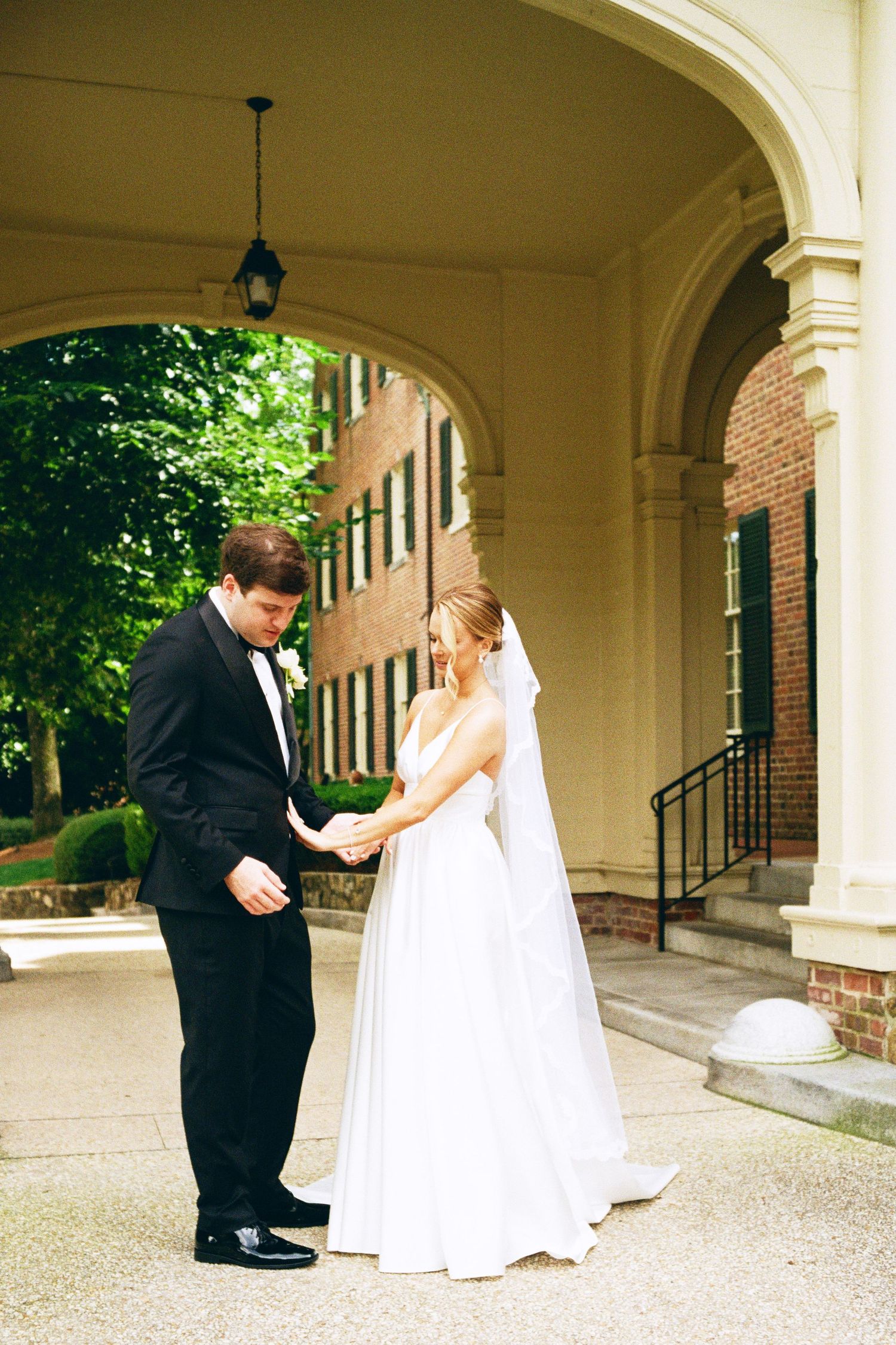 Romantic wedding moment captured under elegant archway with bride in white gown and groom in black tuxedo.