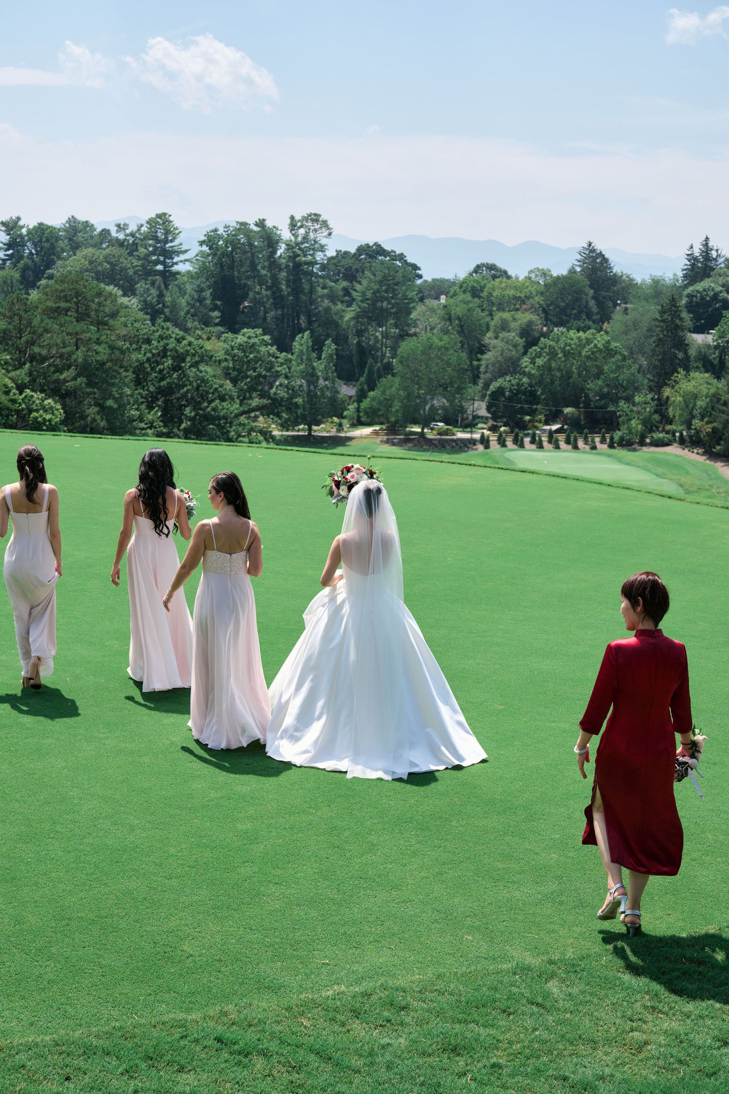 A wedding party walking across a scenic golf course with bridesmaids in pink dresses on a sunny day.