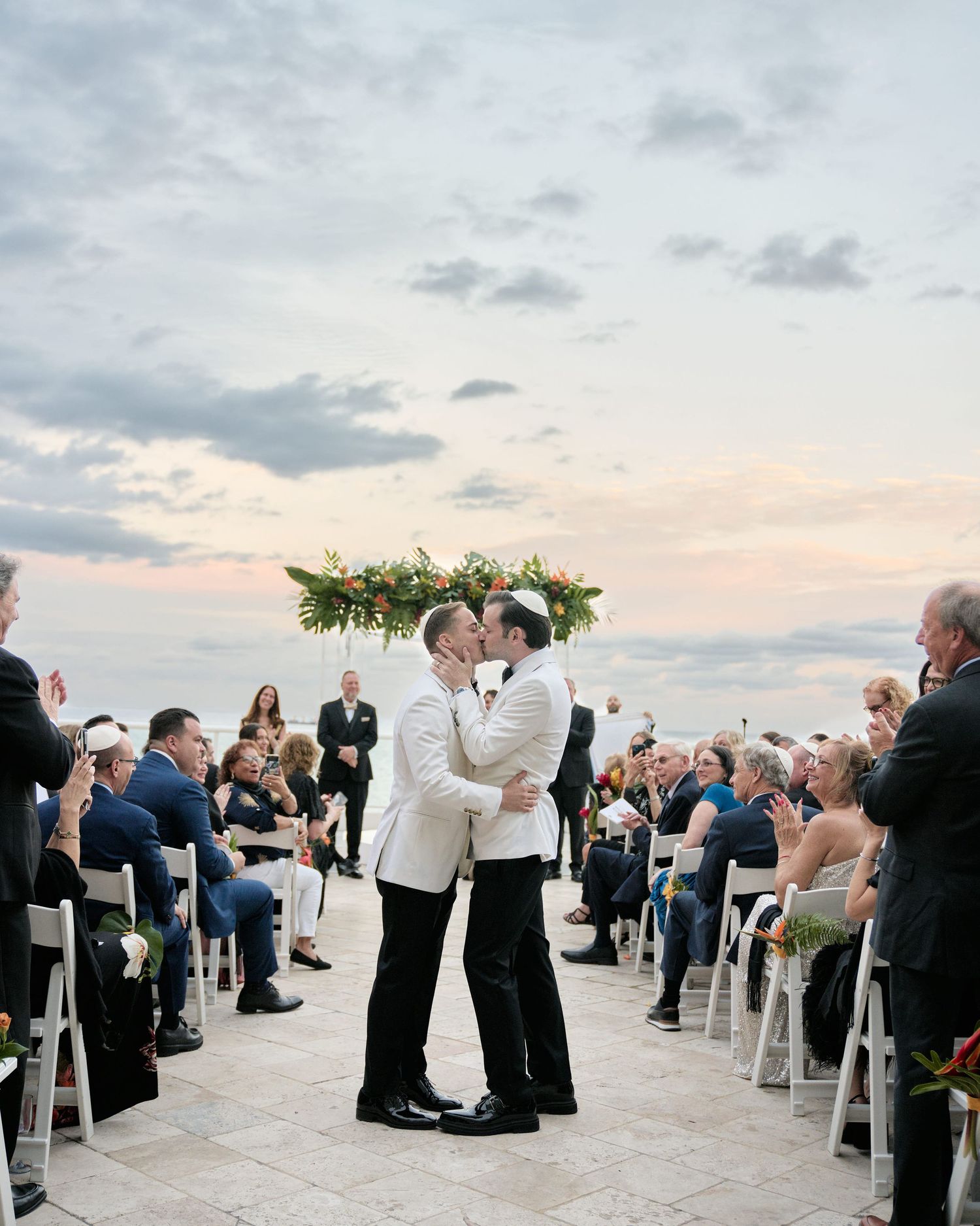 Two people sharing their first kiss as newlyweds during an outdoor ceremony with mountain views at sunset.