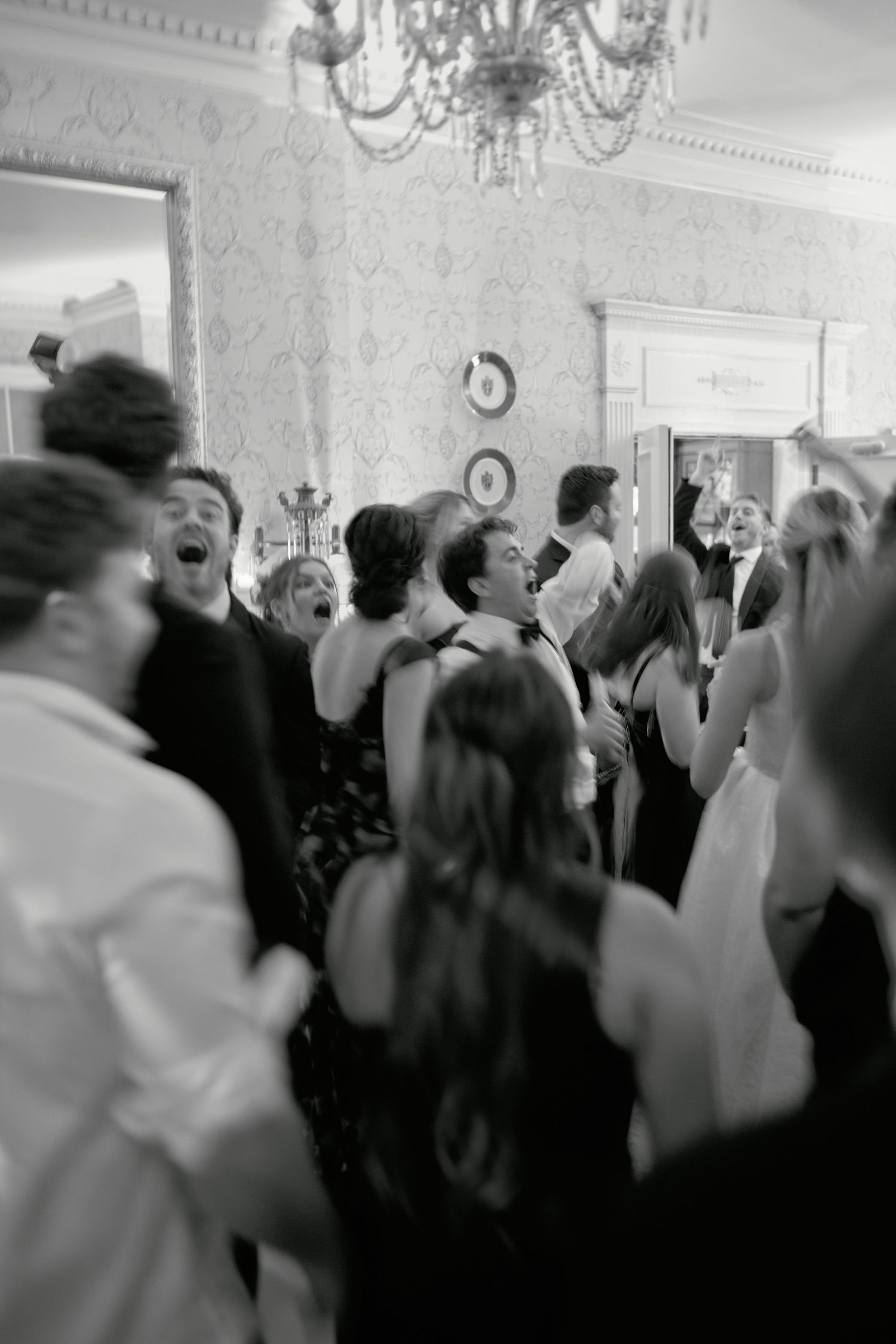 Black and white photo of elegantly dressed guests dancing and celebrating at a formal wedding reception in a grand ballroom.