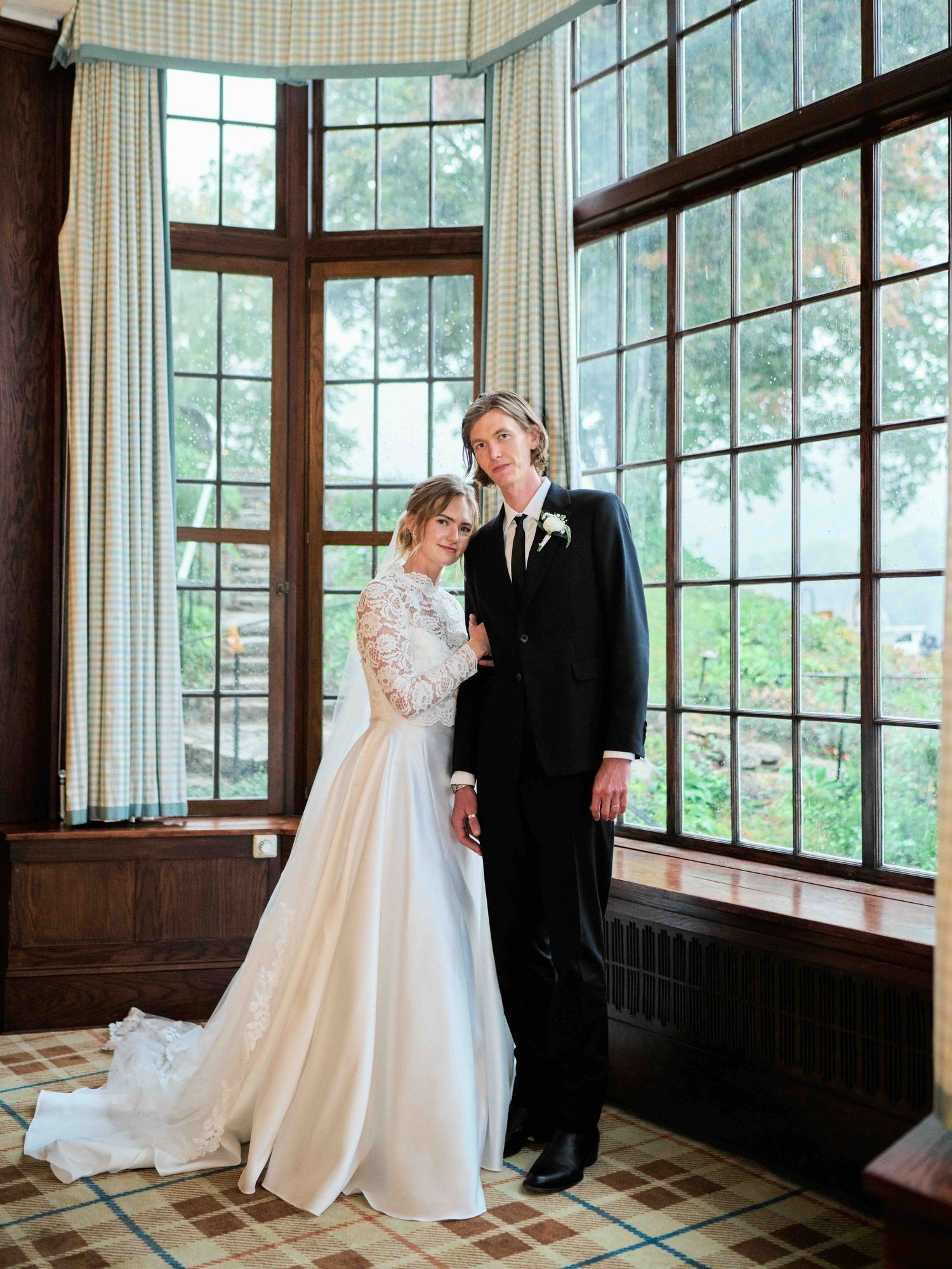 Bride and groom posing elegantly in a sunlit room with large windows on their wedding day.
