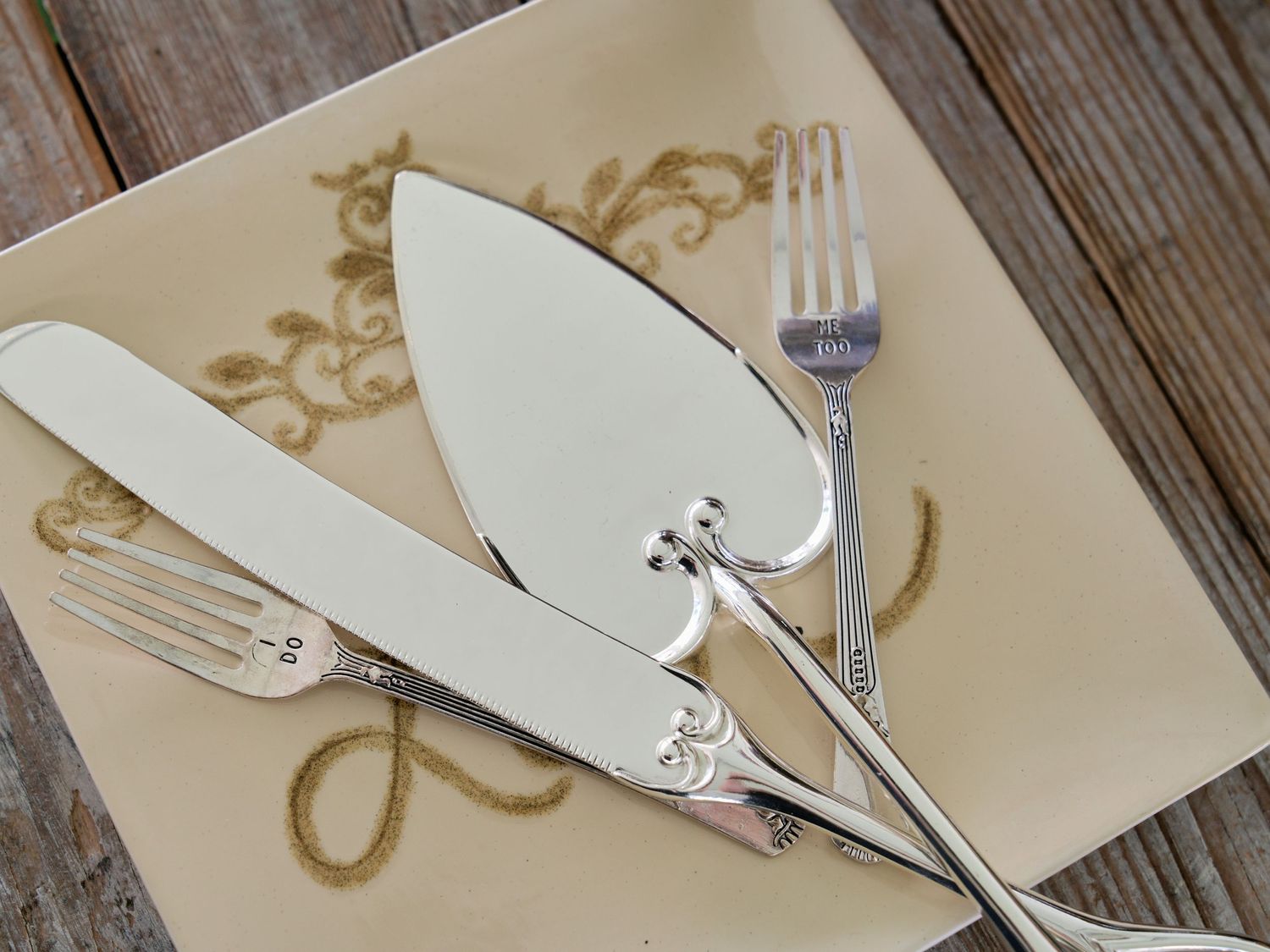 Close-up view of elegant silverware with white ceramic knife and fork on cream colored plate with gold design.