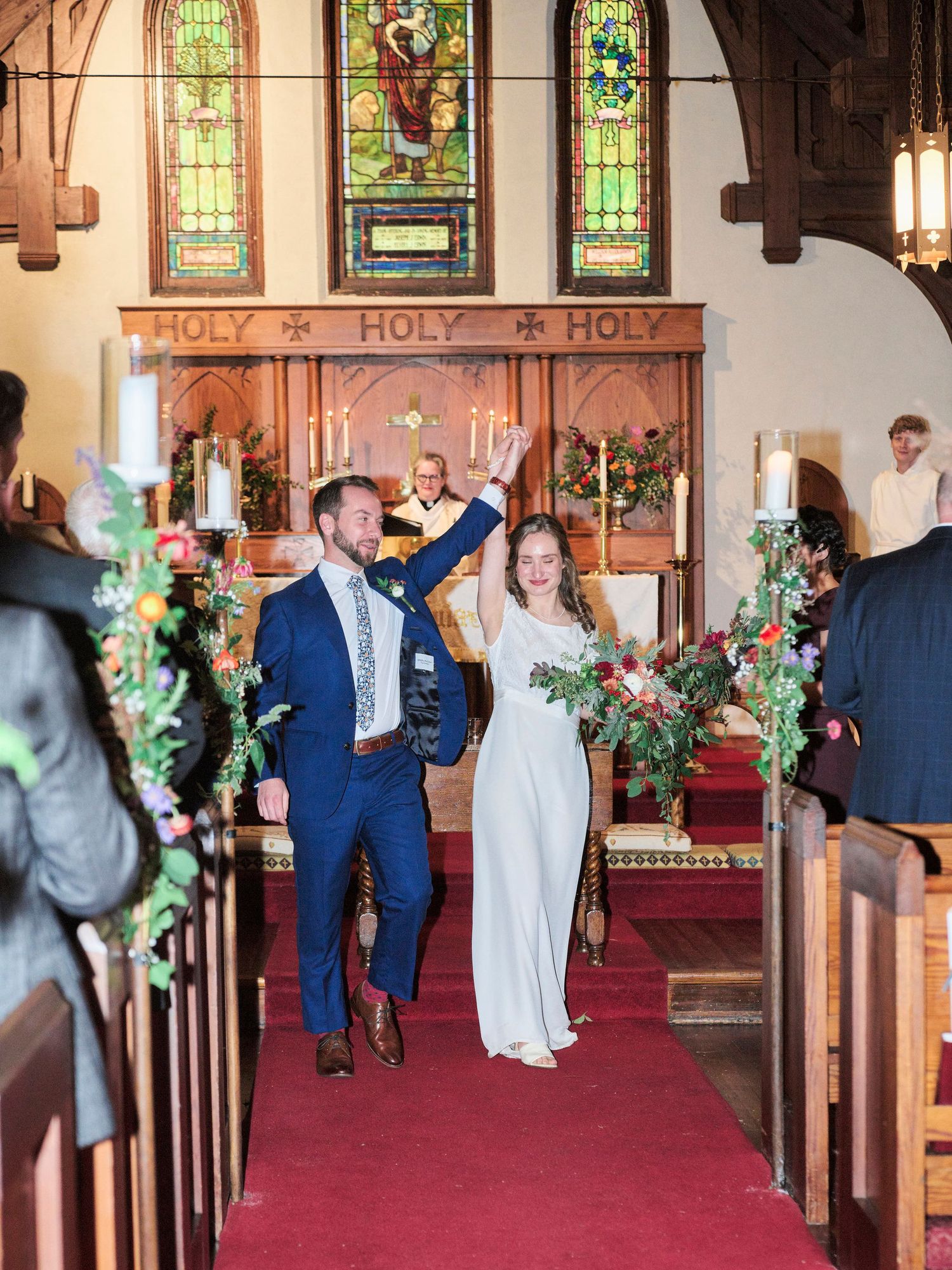 A joyful celebration inside a church with decorative floral arrangements lining the aisle.