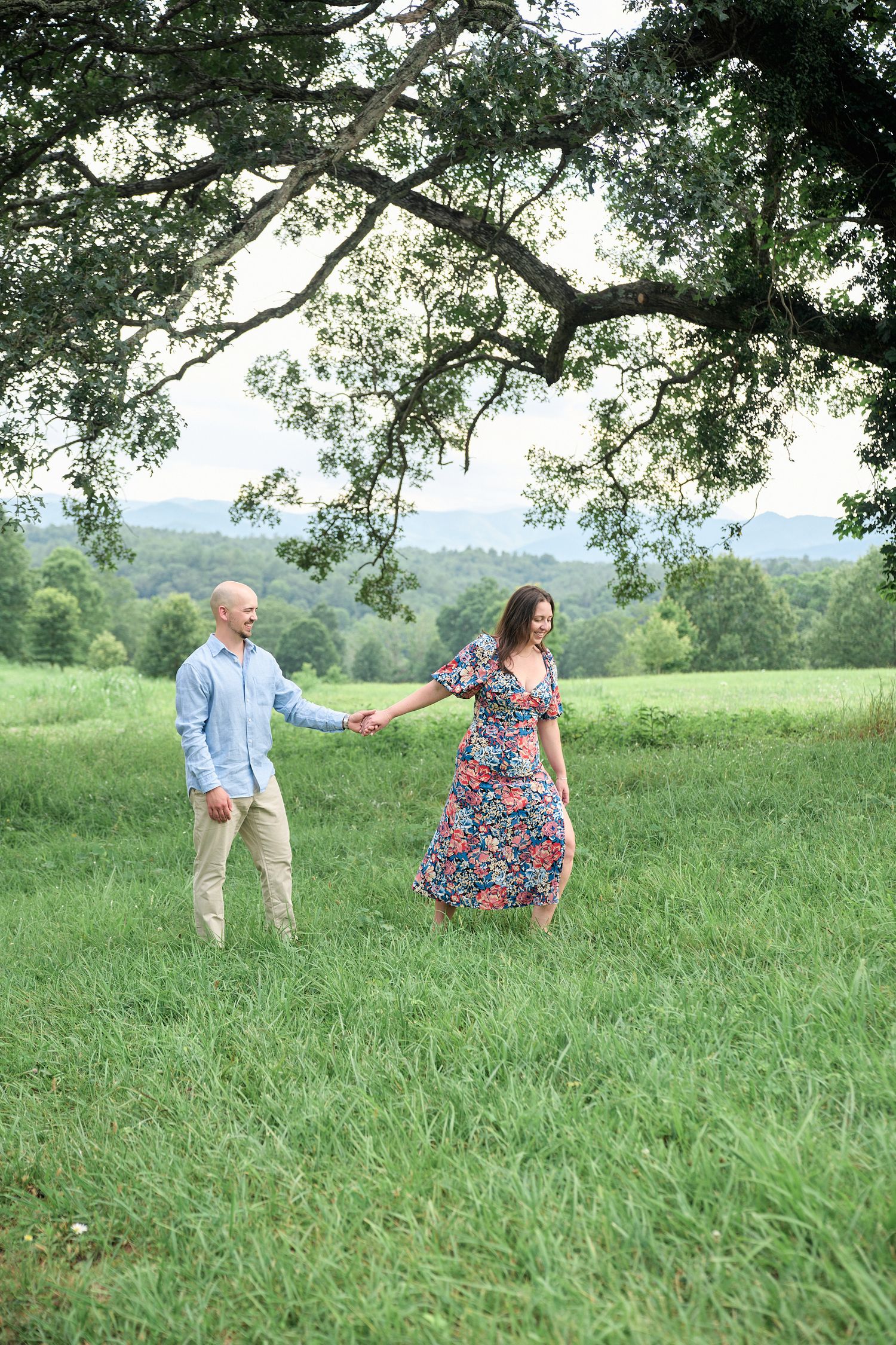 Couple holding hands while dancing in grassy mountain meadow.
