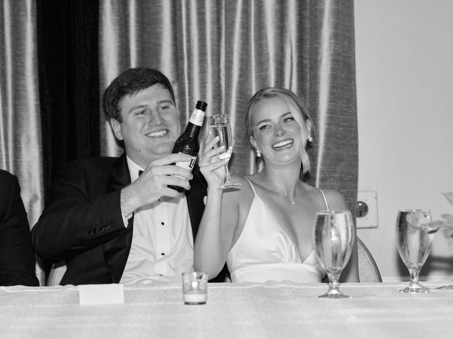 A black and white photo of a couple raising glasses and smiling during a formal celebration toast.