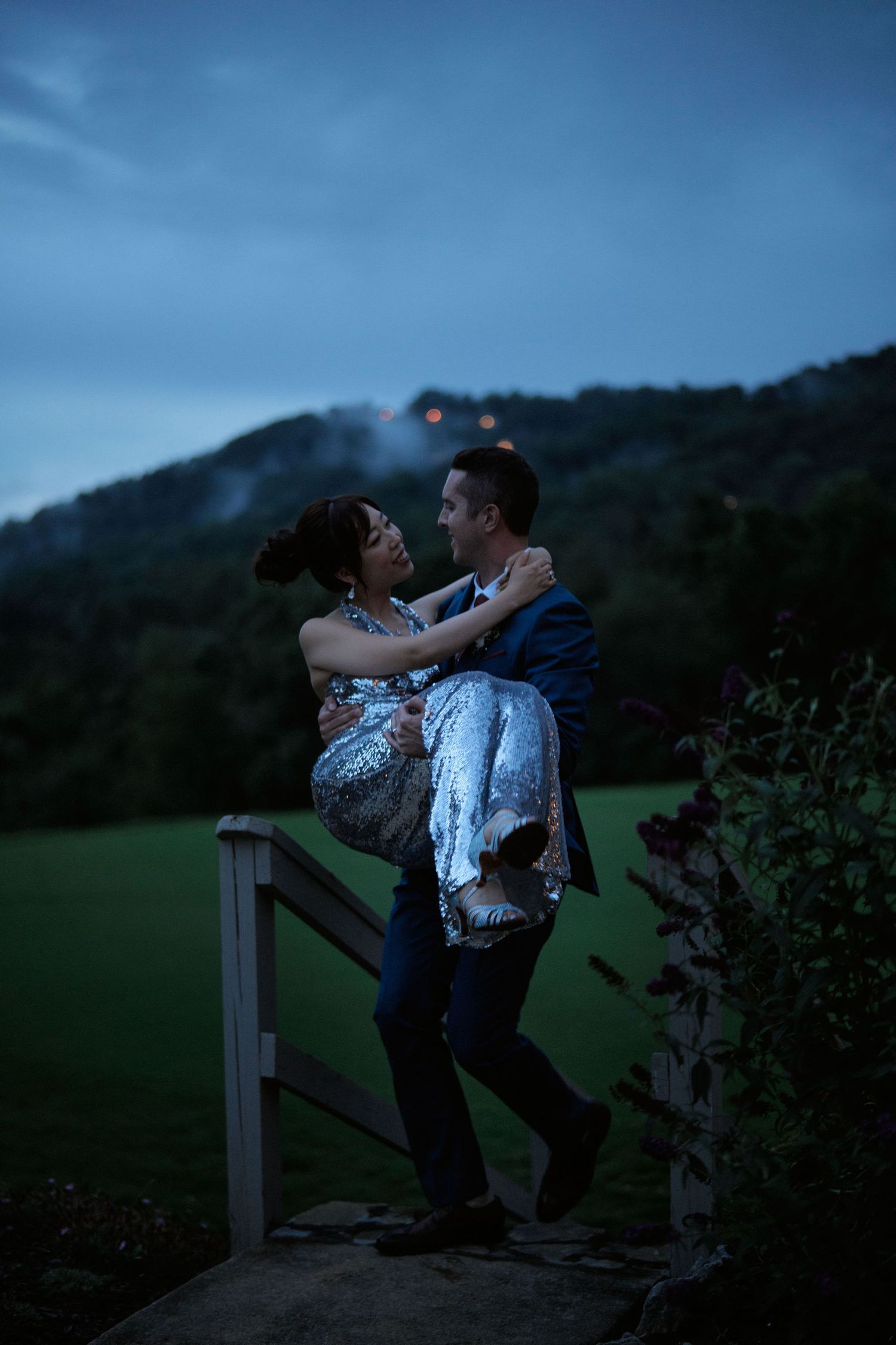 A romantic twilight moment as a couple embraces on a wooden platform with mountains in the background.