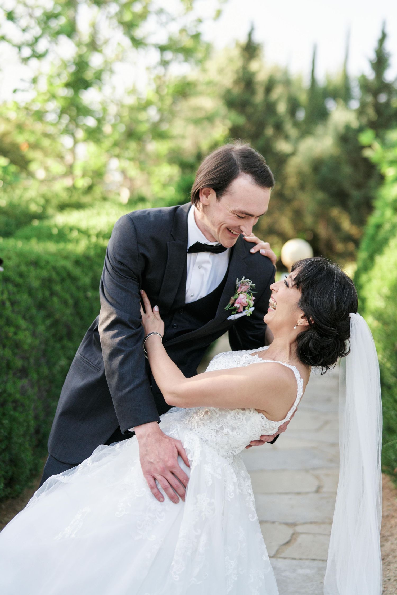 A playful dip pose between newlyweds surrounded by garden greenery.