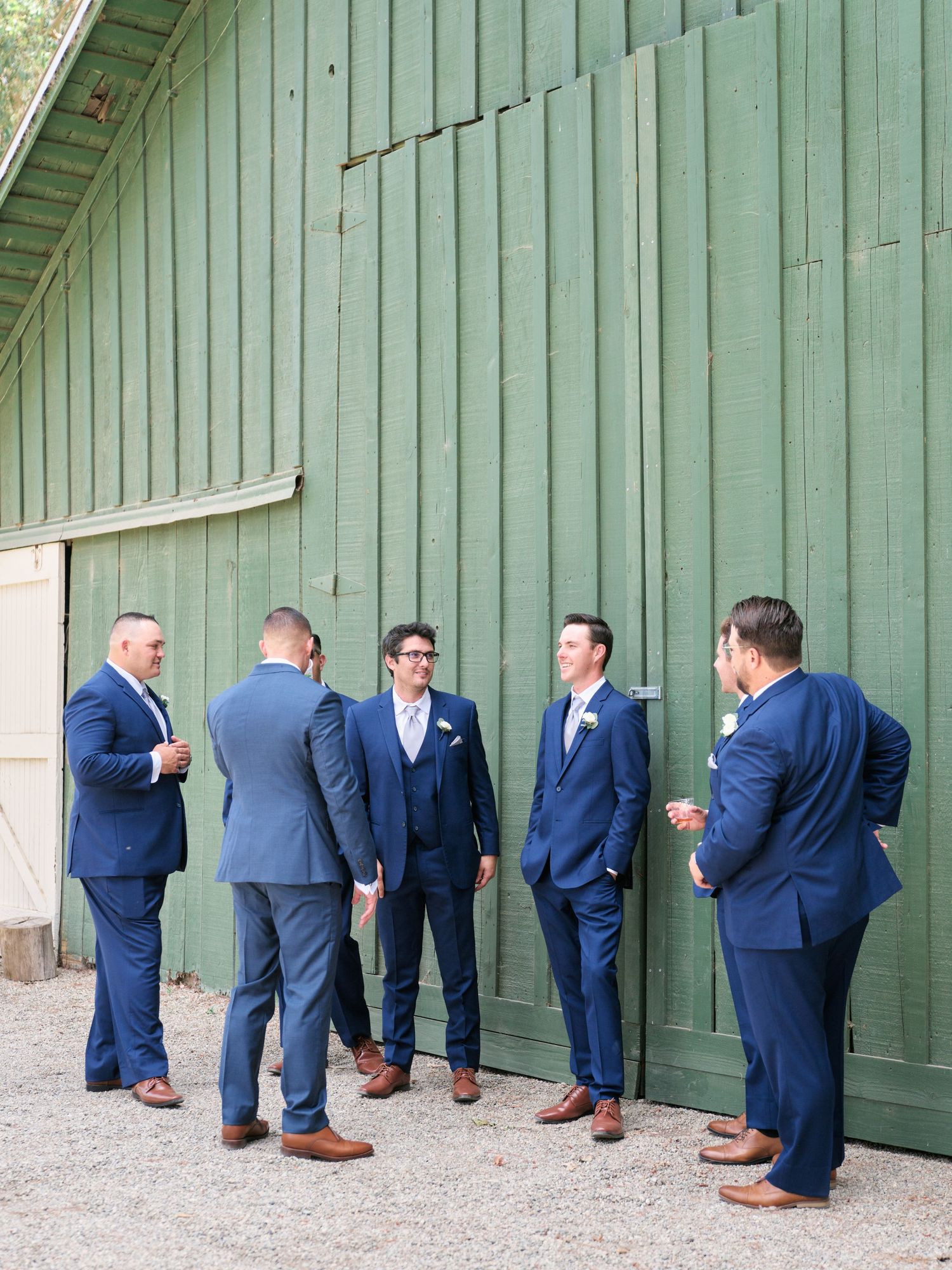 Wedding party in navy suits gathered against a mint green wooden wall.