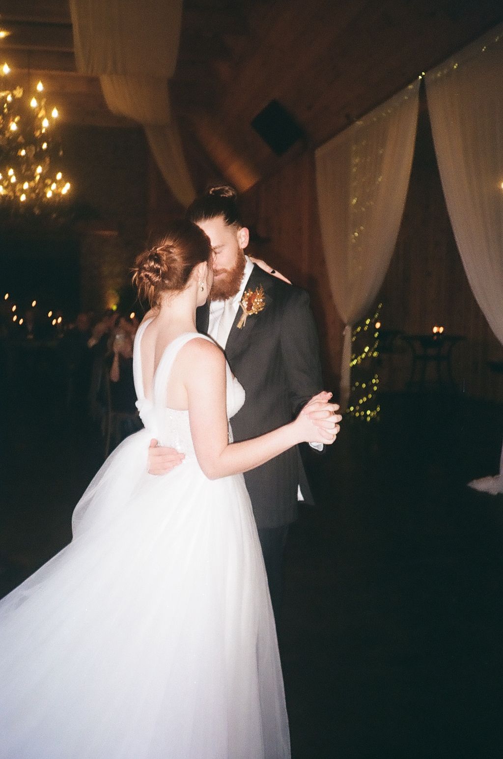 Couple's first dance in elegant ballroom decorated with twinkling lights and white draping.