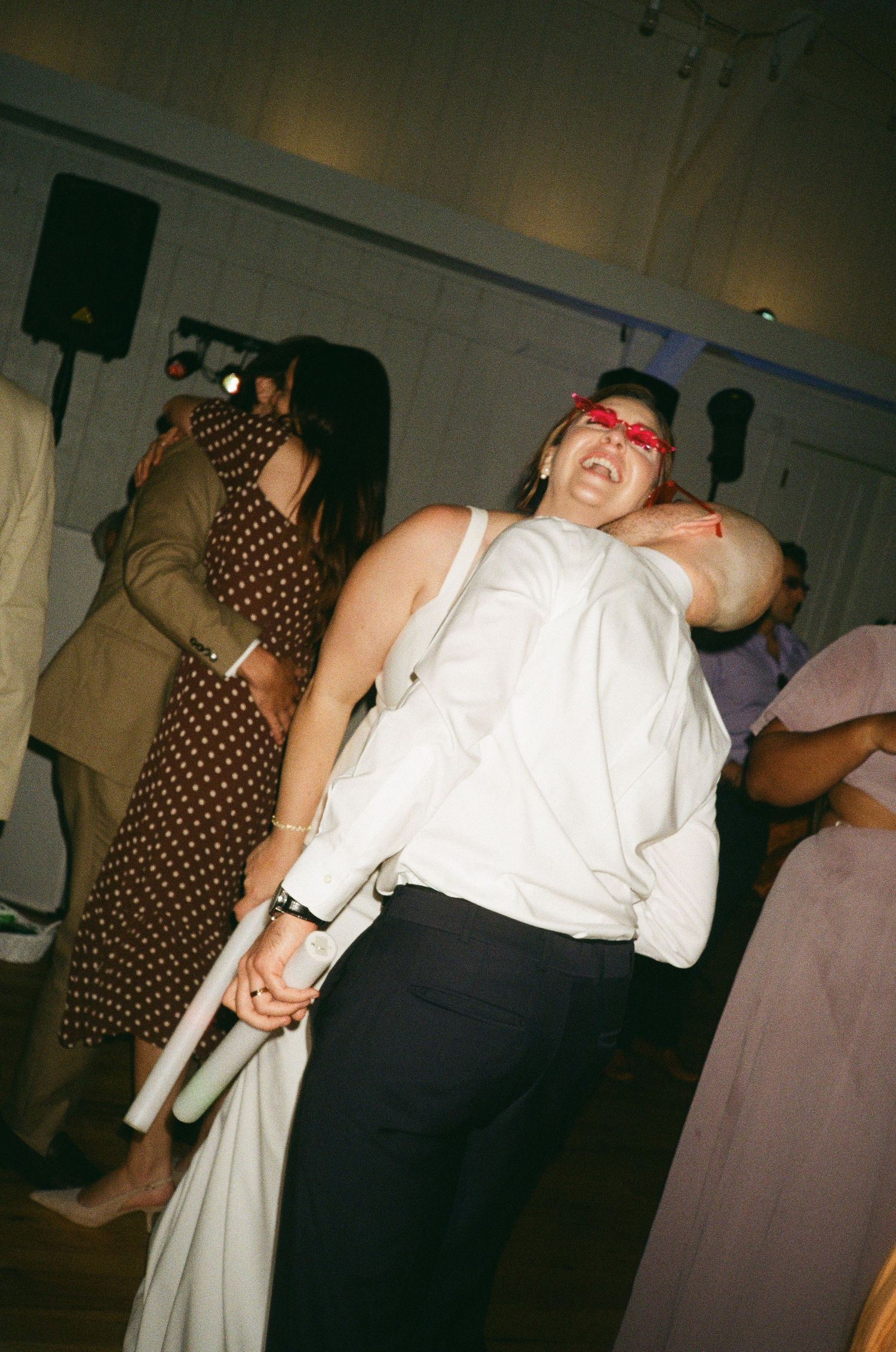 Person dancing energetically at a wedding reception wearing a white shirt and red blindfold accessory.