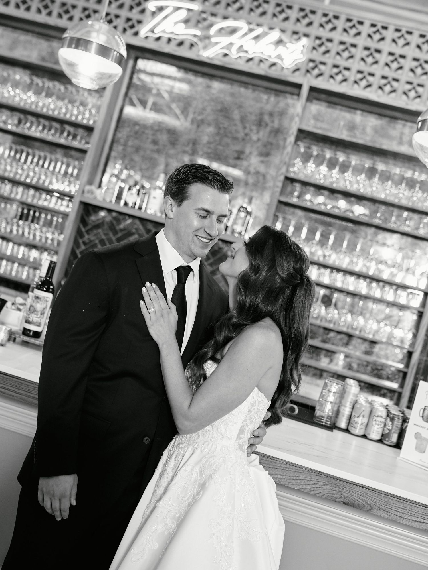 A romantic wedding couple shares intimate moments in a vintage-style bar setting with ornate decor and glass displays.