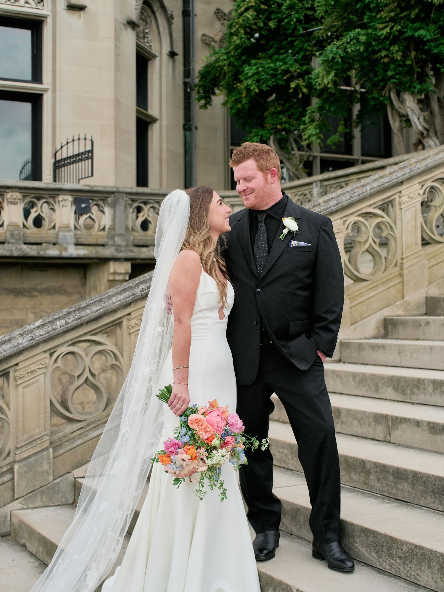 A bride and groom share a romantic moment on an elegant stone staircase during their wedding photo session.