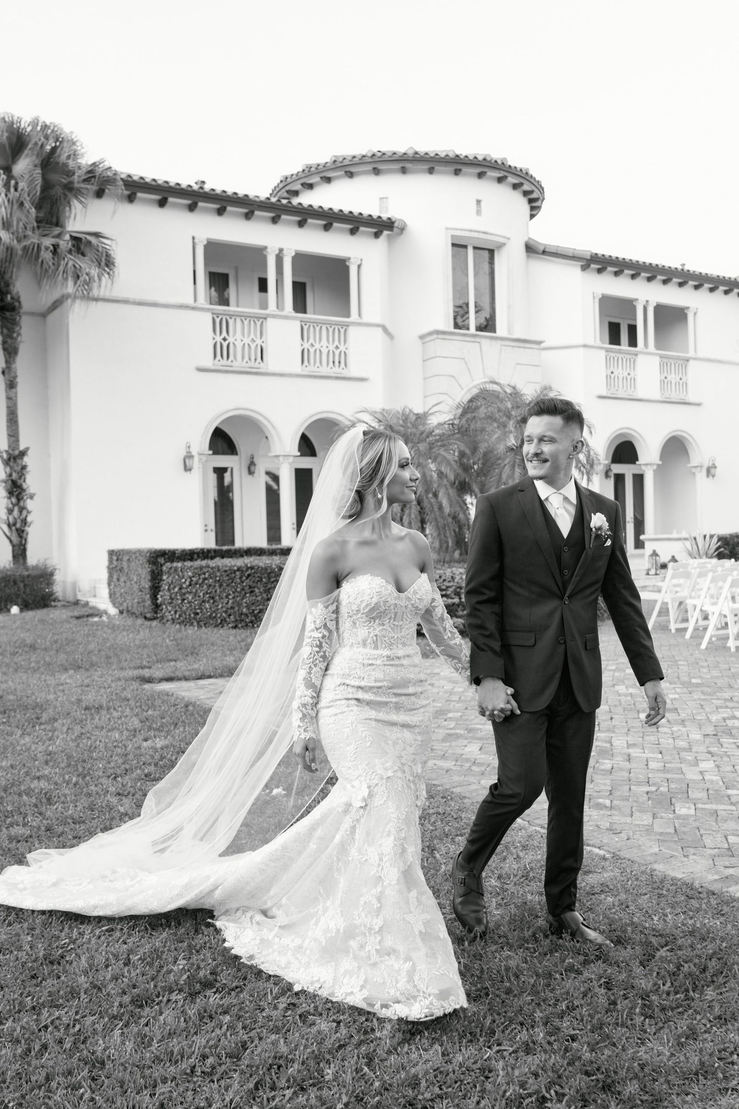Black and white photo of newlyweds walking together outside Mediterranean-style venue.