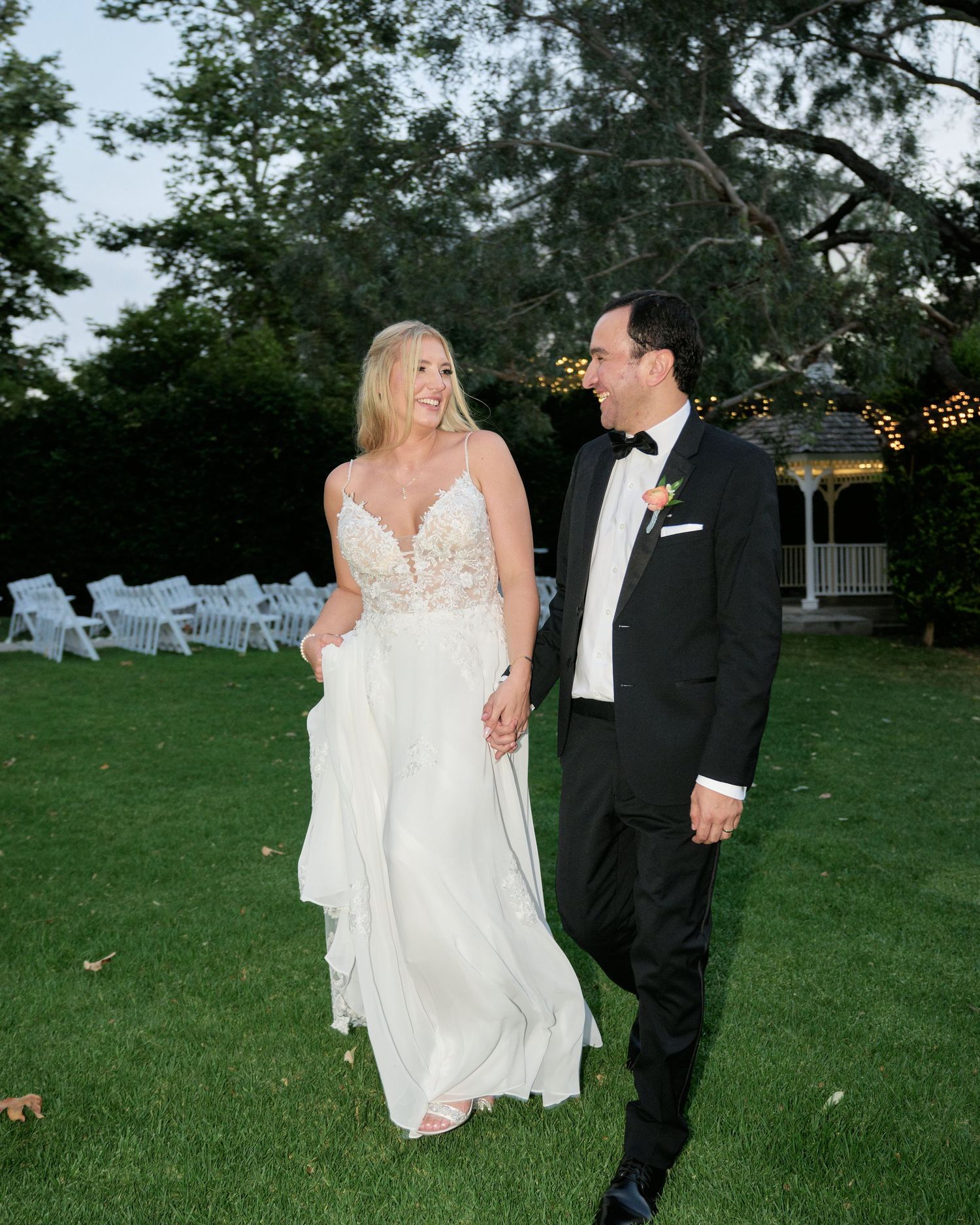 A joyful moment captured between newlyweds walking on grass with string lights visible in background.