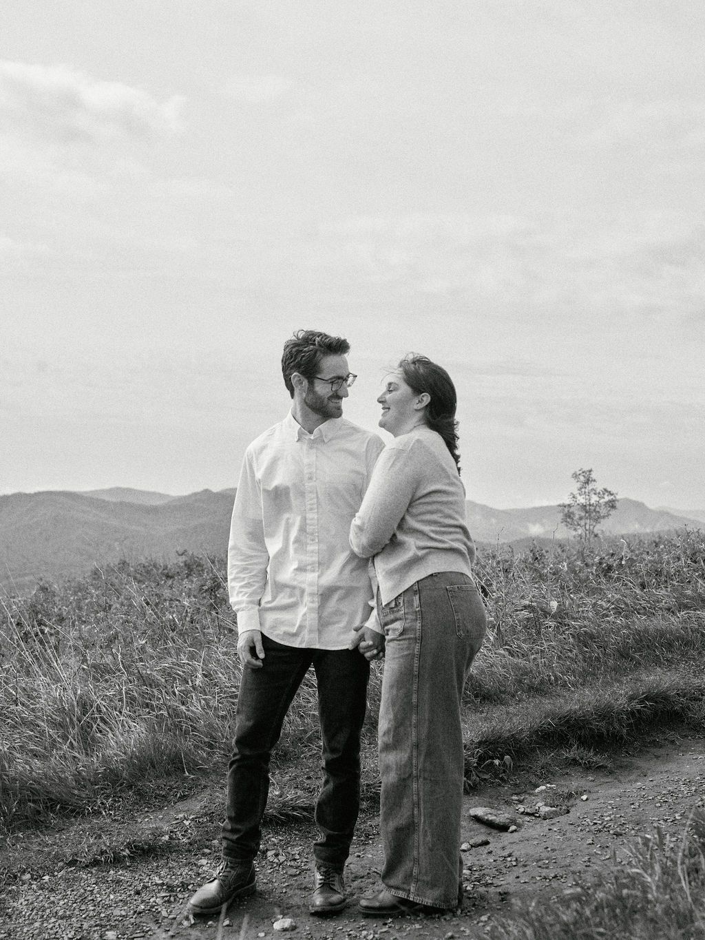 A couple shares a tender moment together on a hillside path in black and white photography.