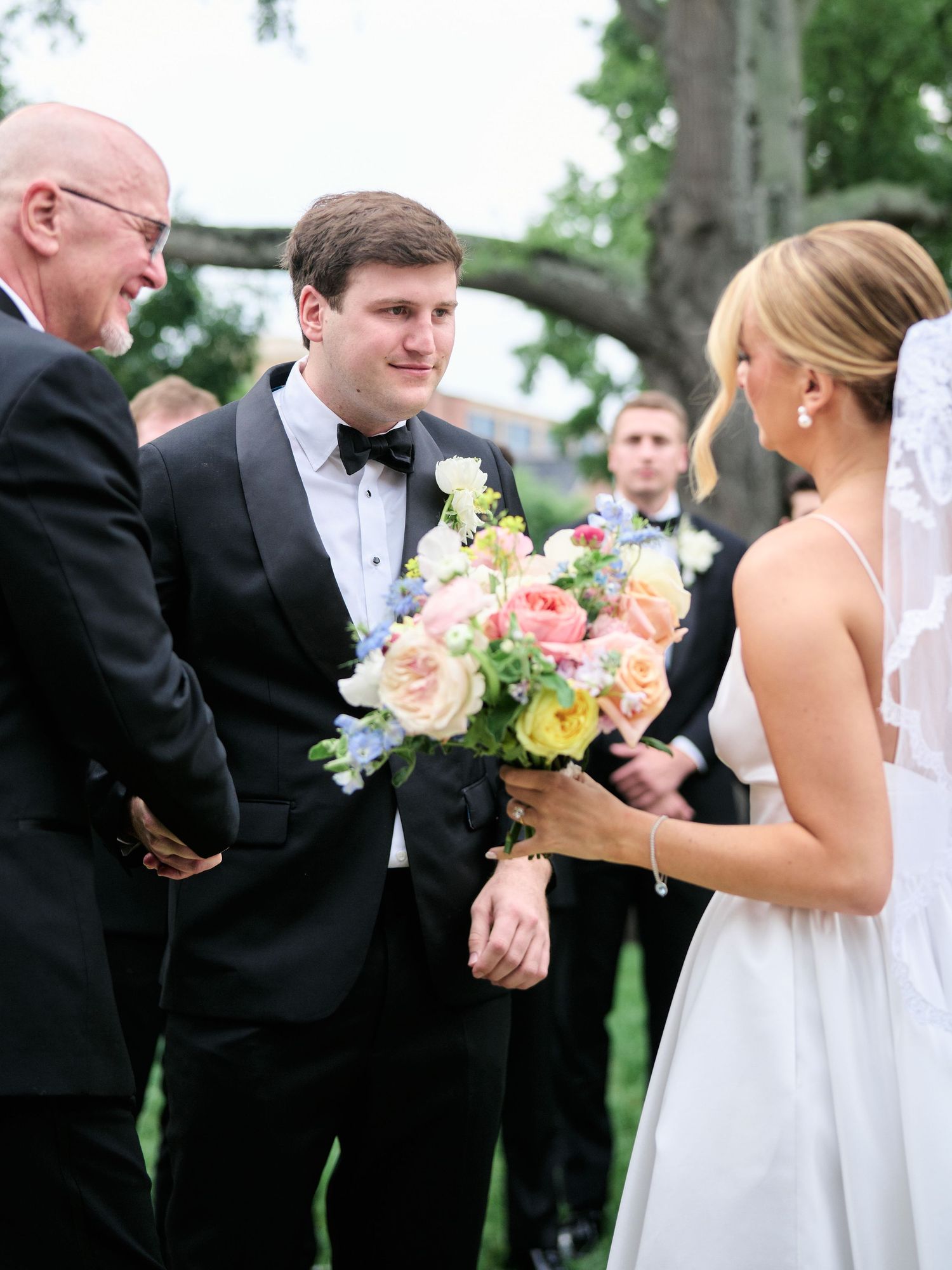 Wedding party gathered under tree branches with elegant floral arrangements.
