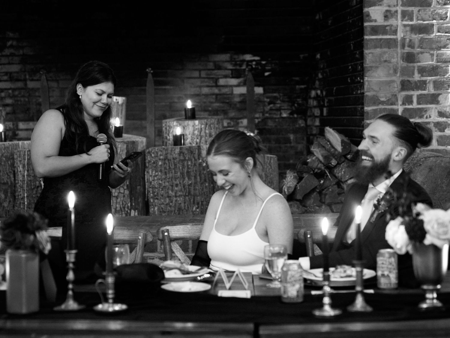 Wedding guests enjoy dinner and conversation at a candlelit reception with exposed brick walls.