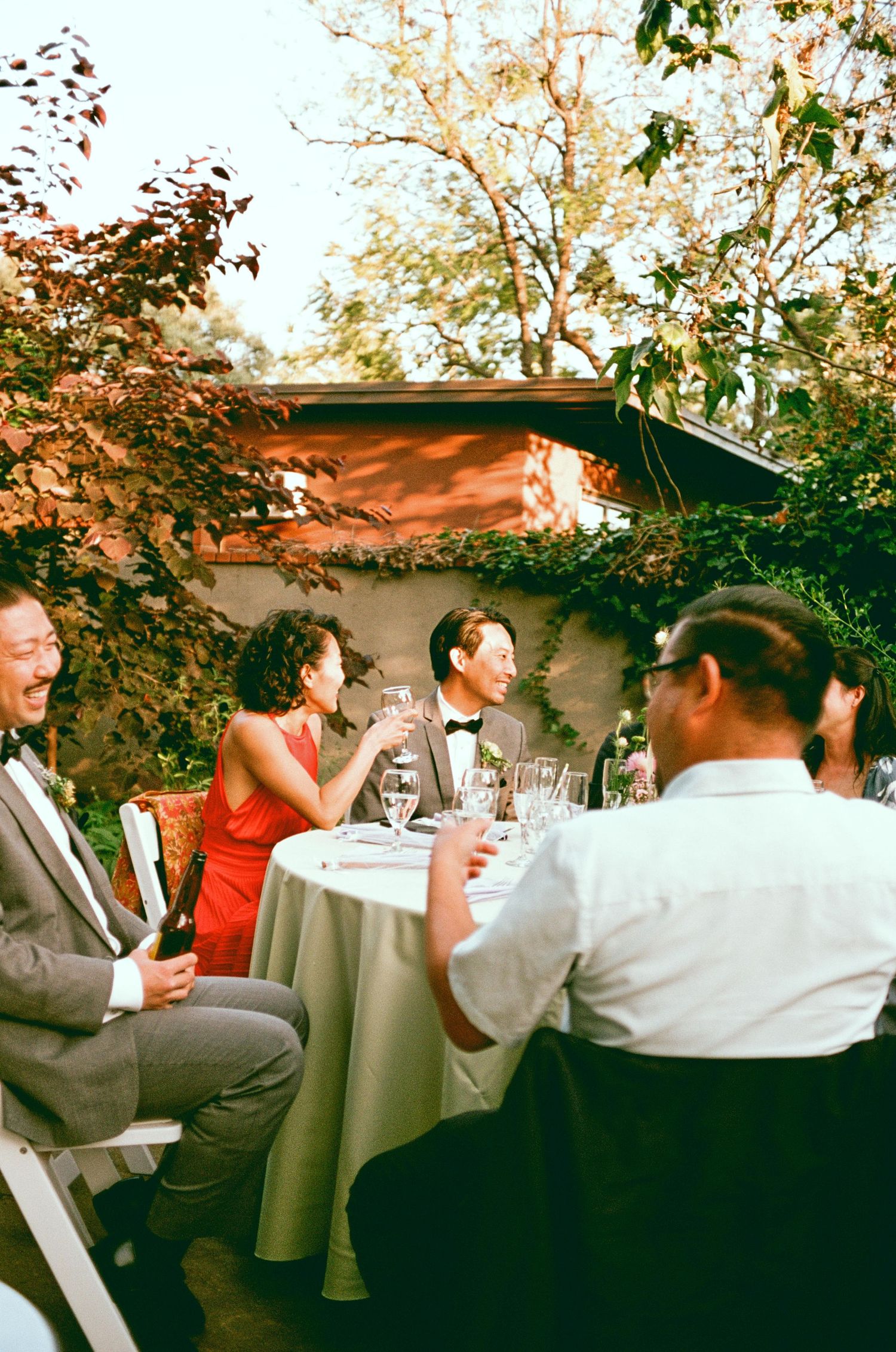 Wedding guests enjoying outdoor reception dinner under natural lighting.