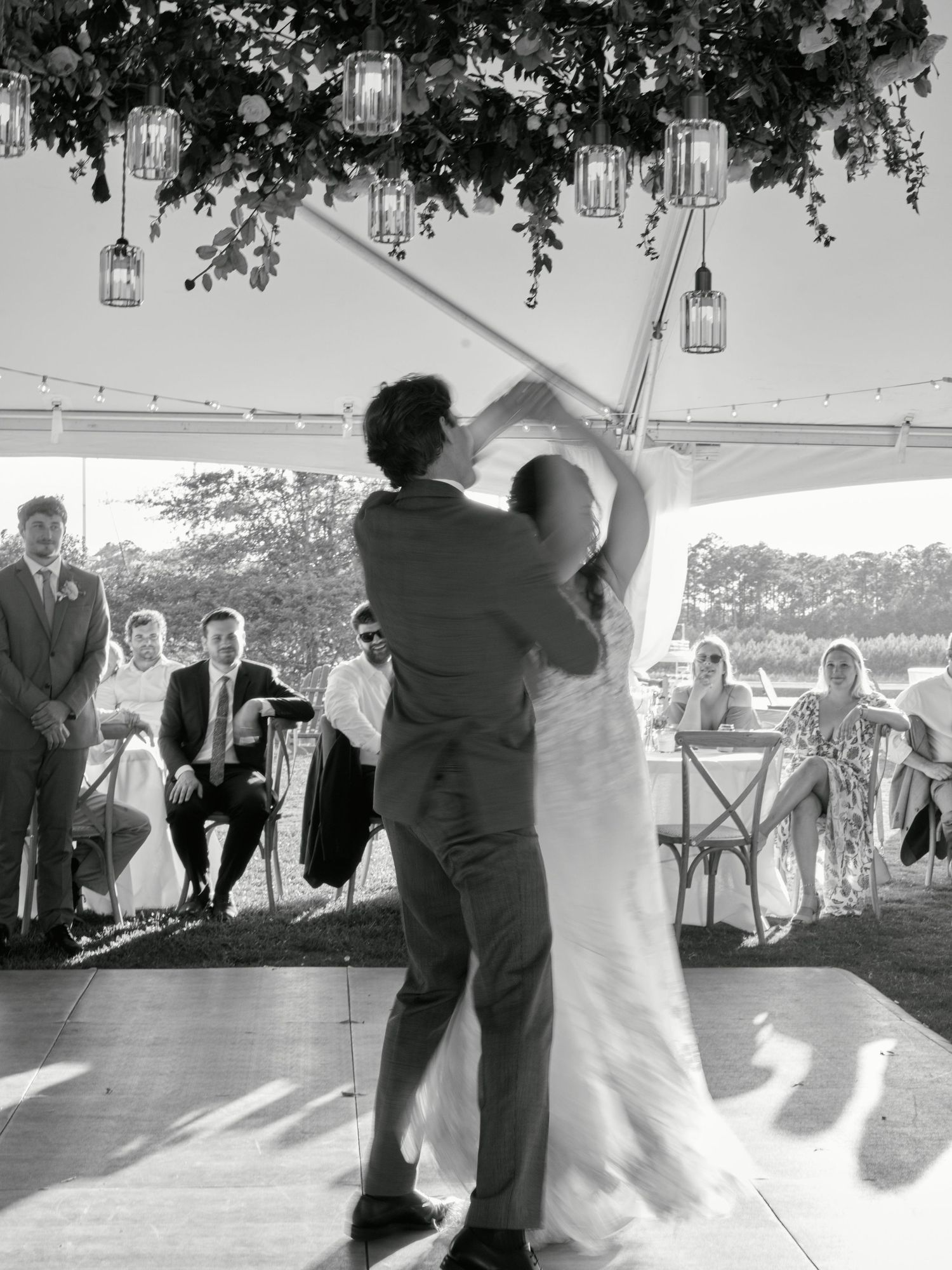 A couple shares their first dance under a tent decorated with hanging lanterns at an outdoor wedding reception.
