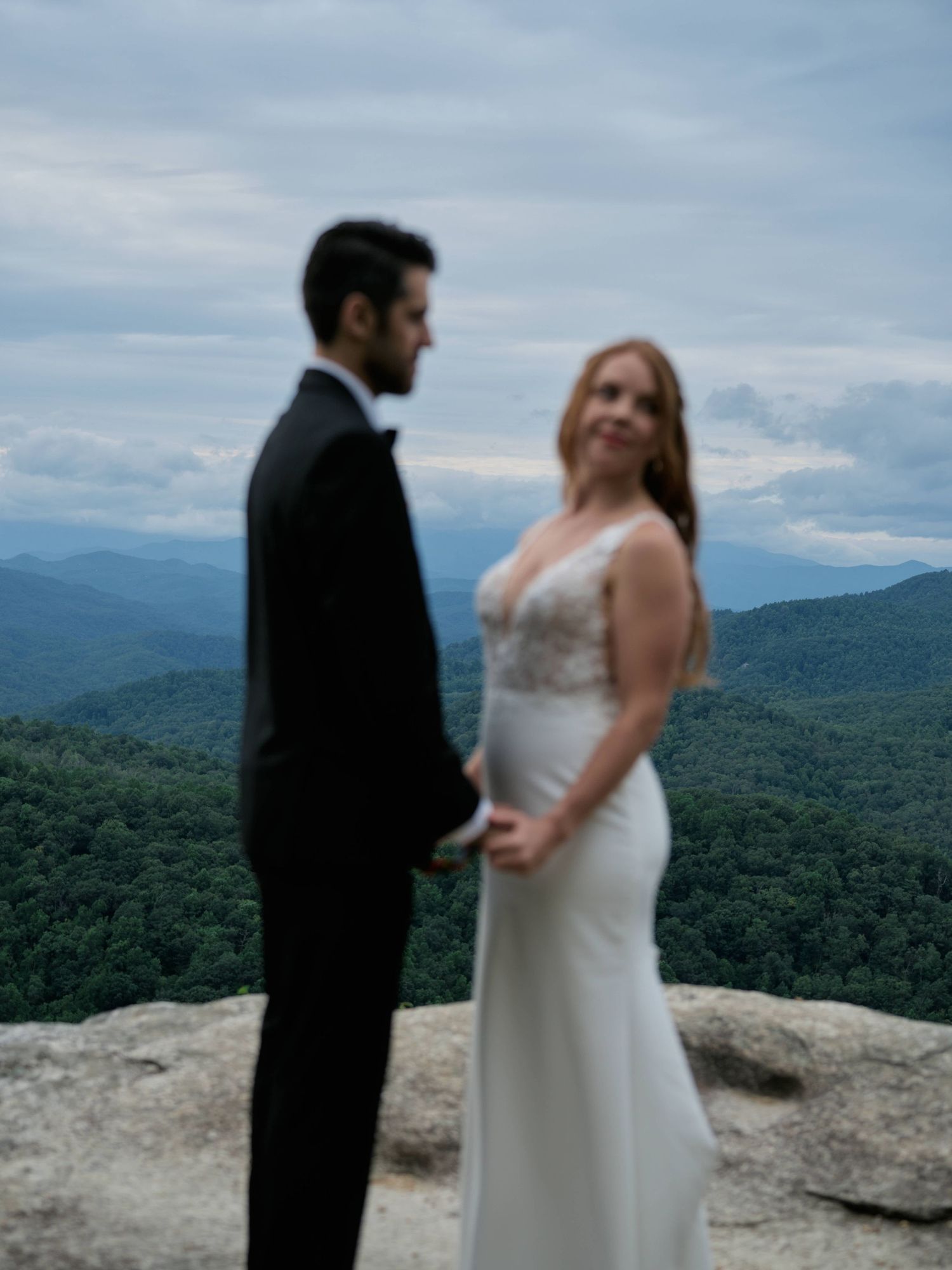 A couple shares an intimate moment during their mountain-top wedding ceremony with stunning forest views in the background.