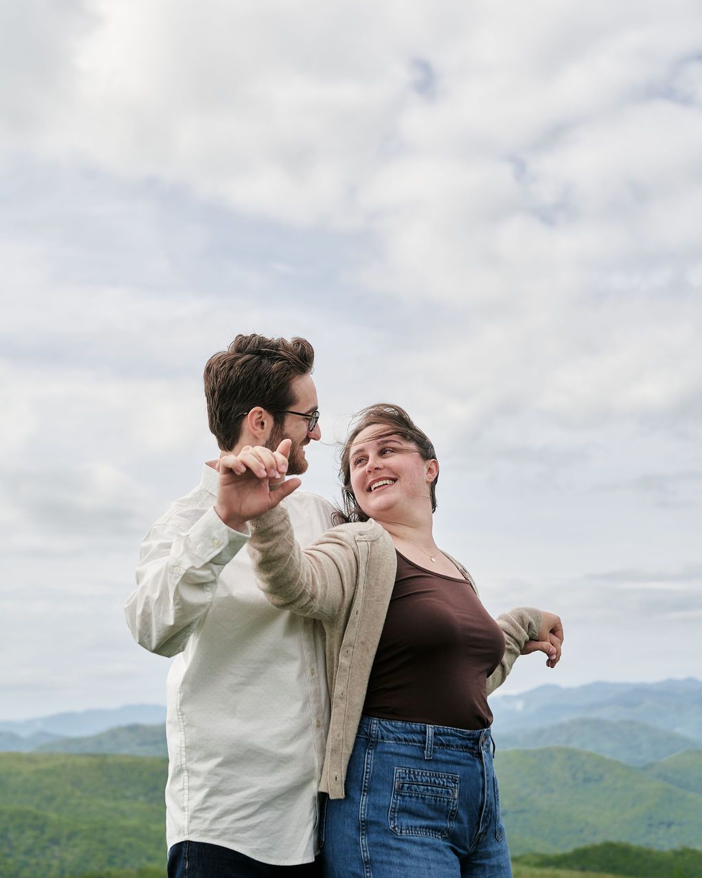 Two people dance together joyfully against a scenic mountain backdrop on an overcast day.