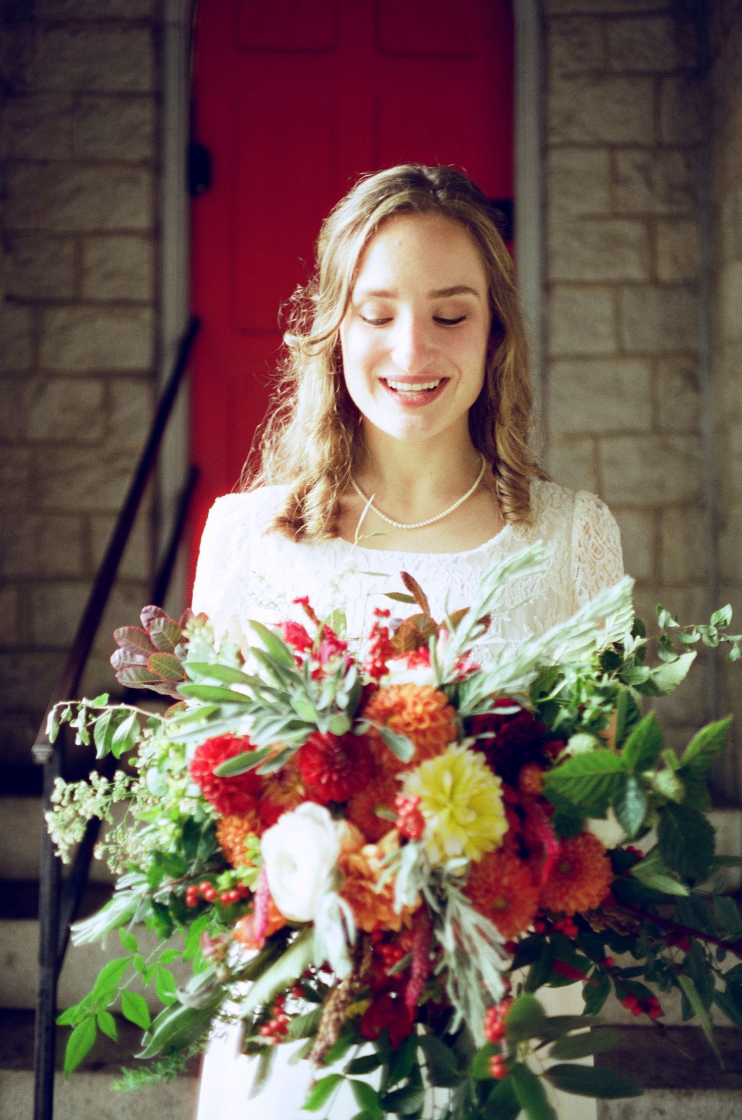 A stunning bridal bouquet features vibrant red and yellow flowers against stone architecture.