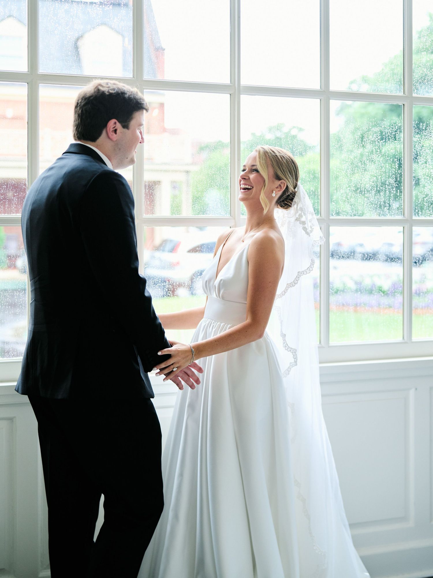 Couple shares joyful moment near large windows in elegant indoor wedding setting.