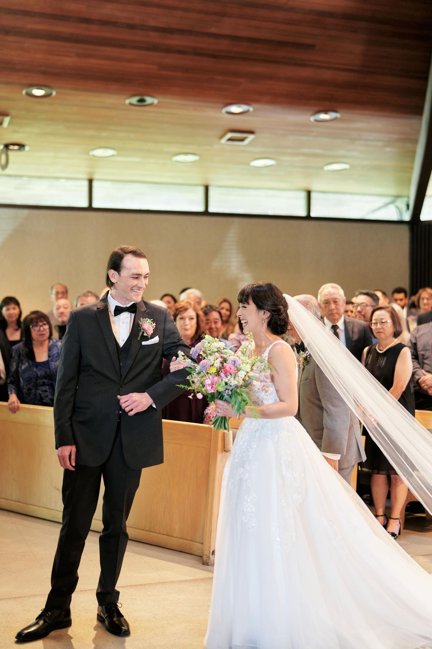 A wedding ceremony in a modern chapel with guests watching the couple exchange vows.