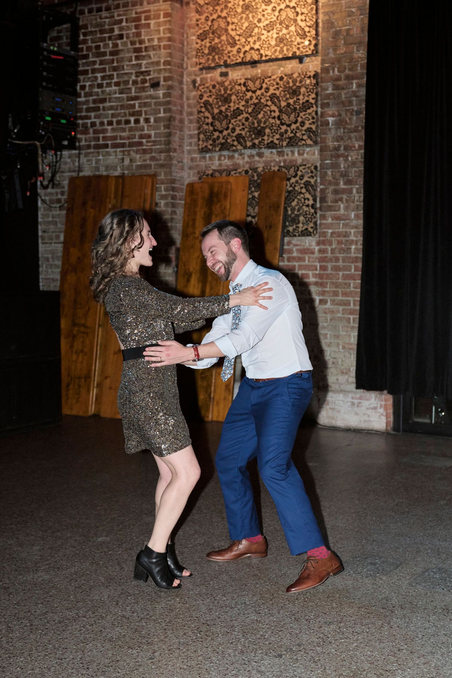 Couple dances together against exposed brick wall at wedding reception.