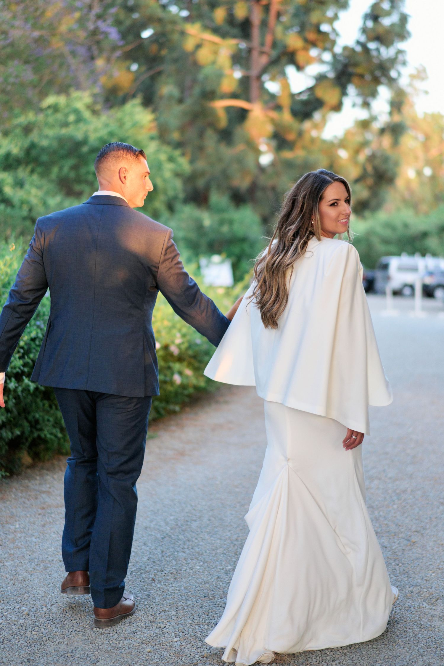 A couple in wedding attire walks along a garden path during their special day.