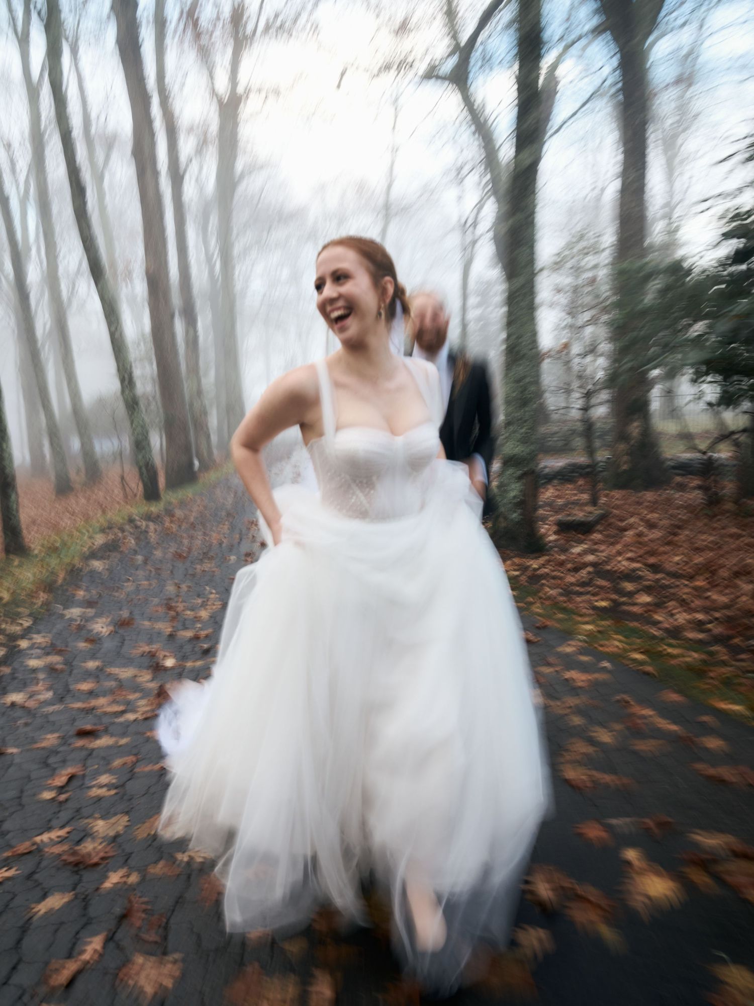 A joyful bride in a flowing white gown twirls in a misty autumn forest.