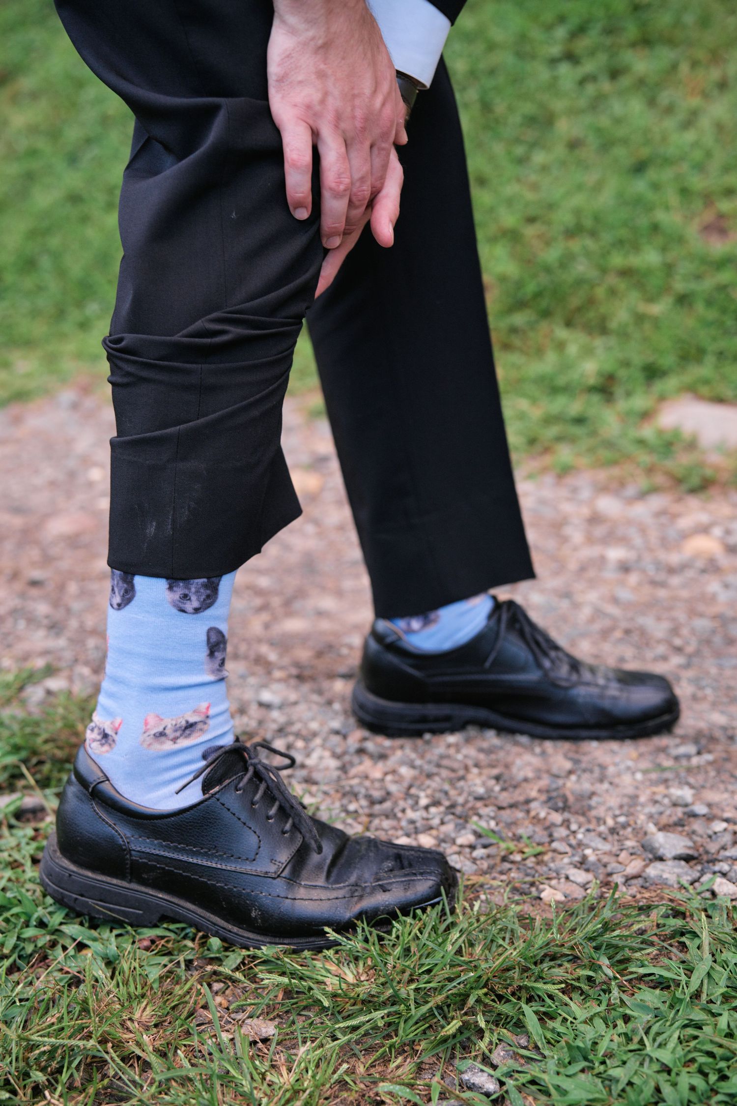 Person wearing light blue cat-print novelty socks with black dress shoes and dark trousers outdoors.