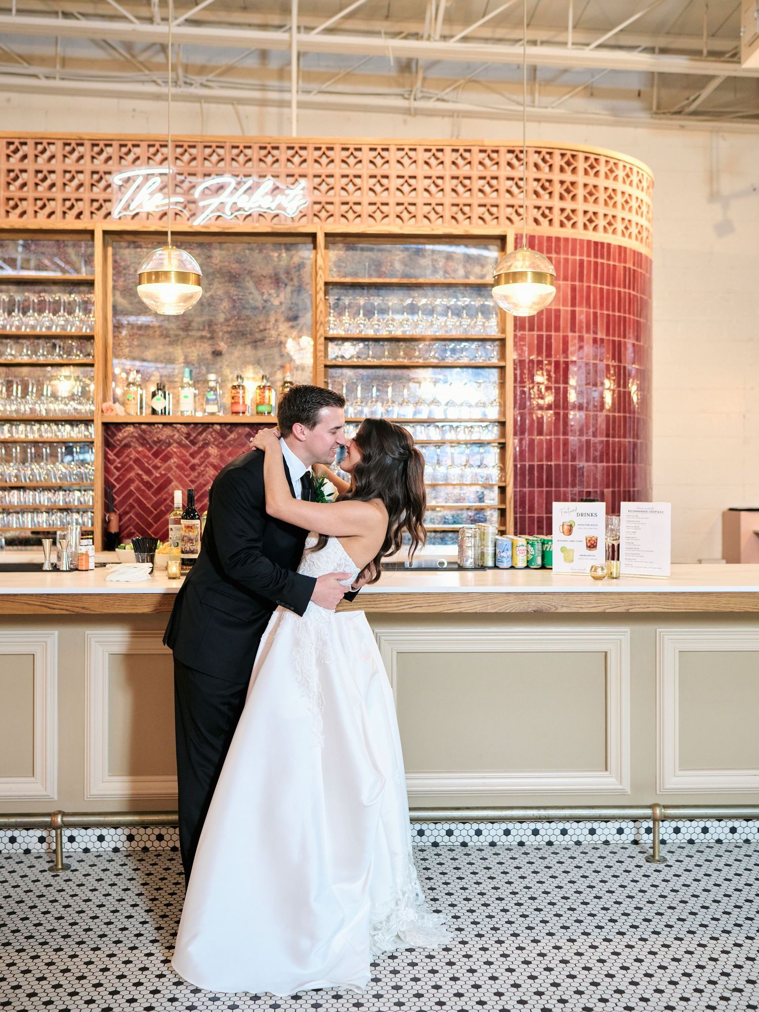 Bride and groom share a romantic kiss in front of an elegant bar backdrop at their wedding reception venue.