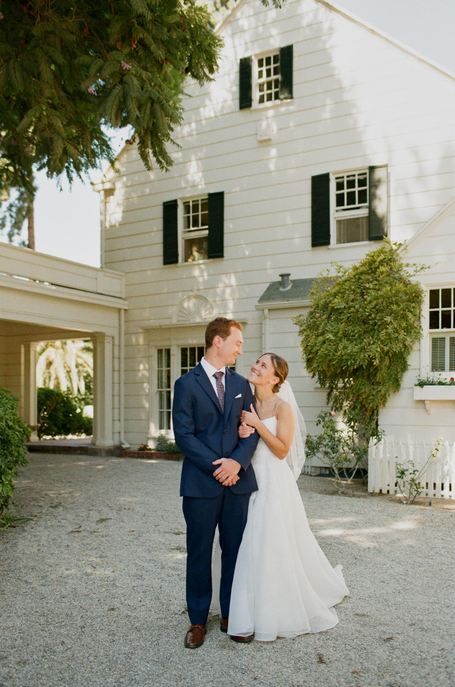 Bride and groom share a romantic moment outside a white colonial-style home on their wedding day.