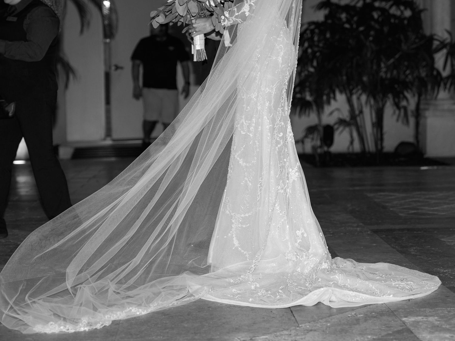 Elegant lace wedding dress with flowing cathedral veil creating a dramatic train on stone floor.