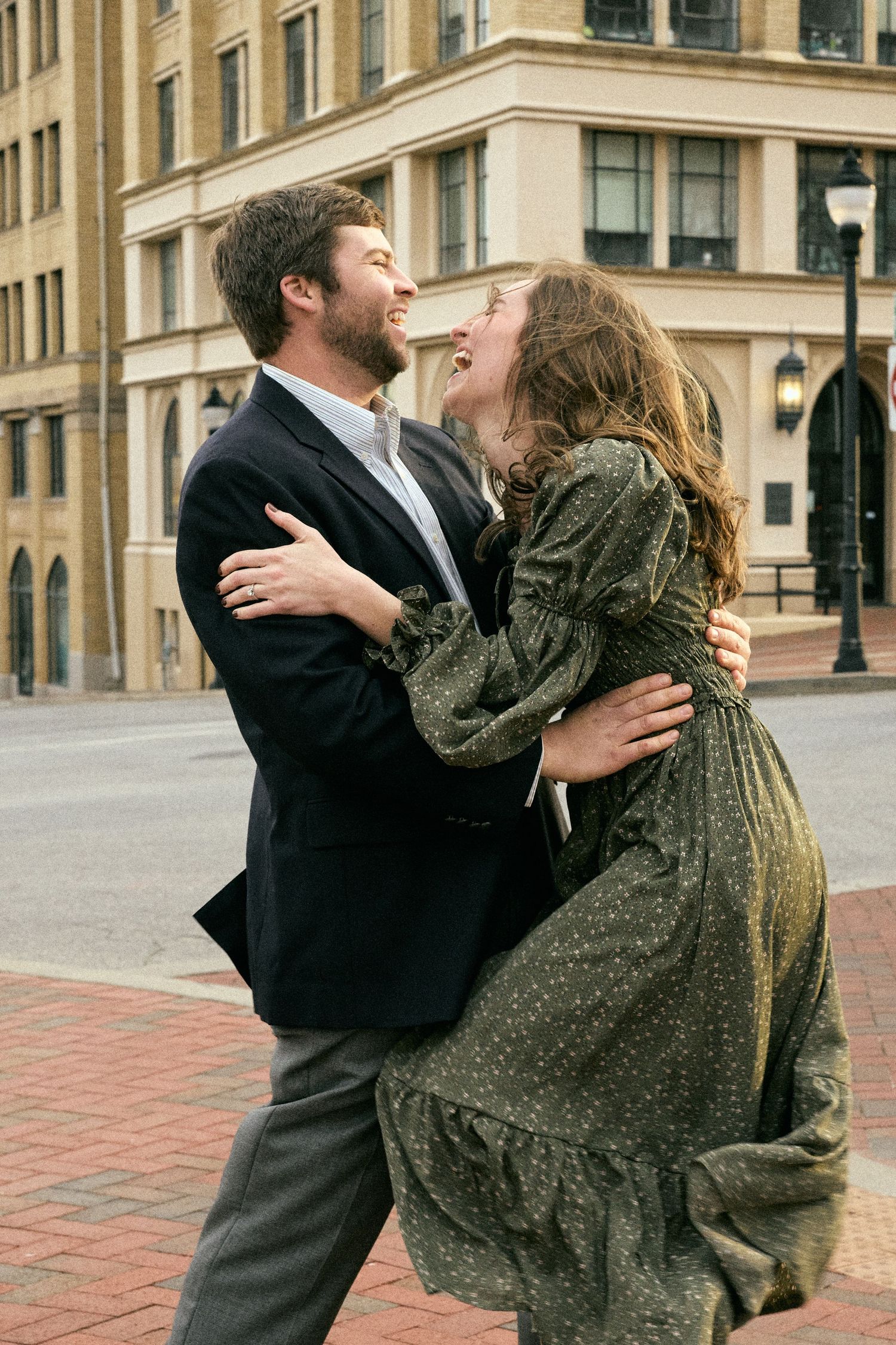 A playful couple laughs and embraces on a city sidewalk.