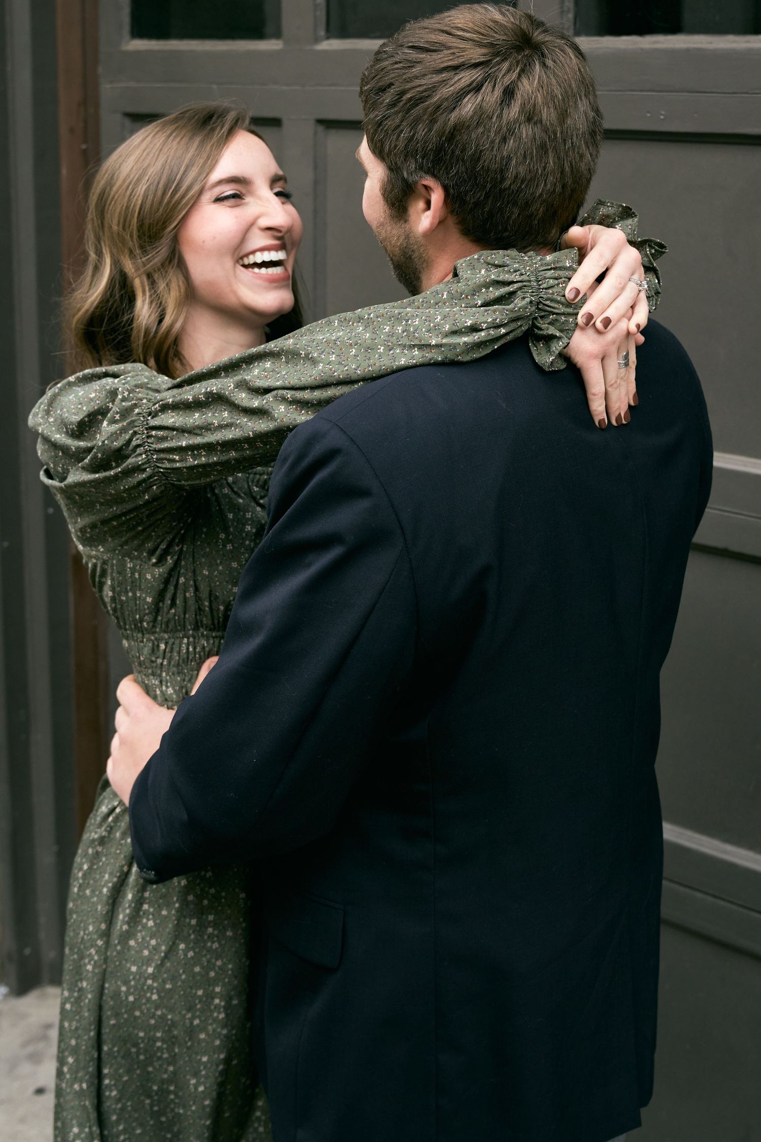 A couple shares a joyful embrace while wearing formal attire, with her in a green dress and him in a dark suit.