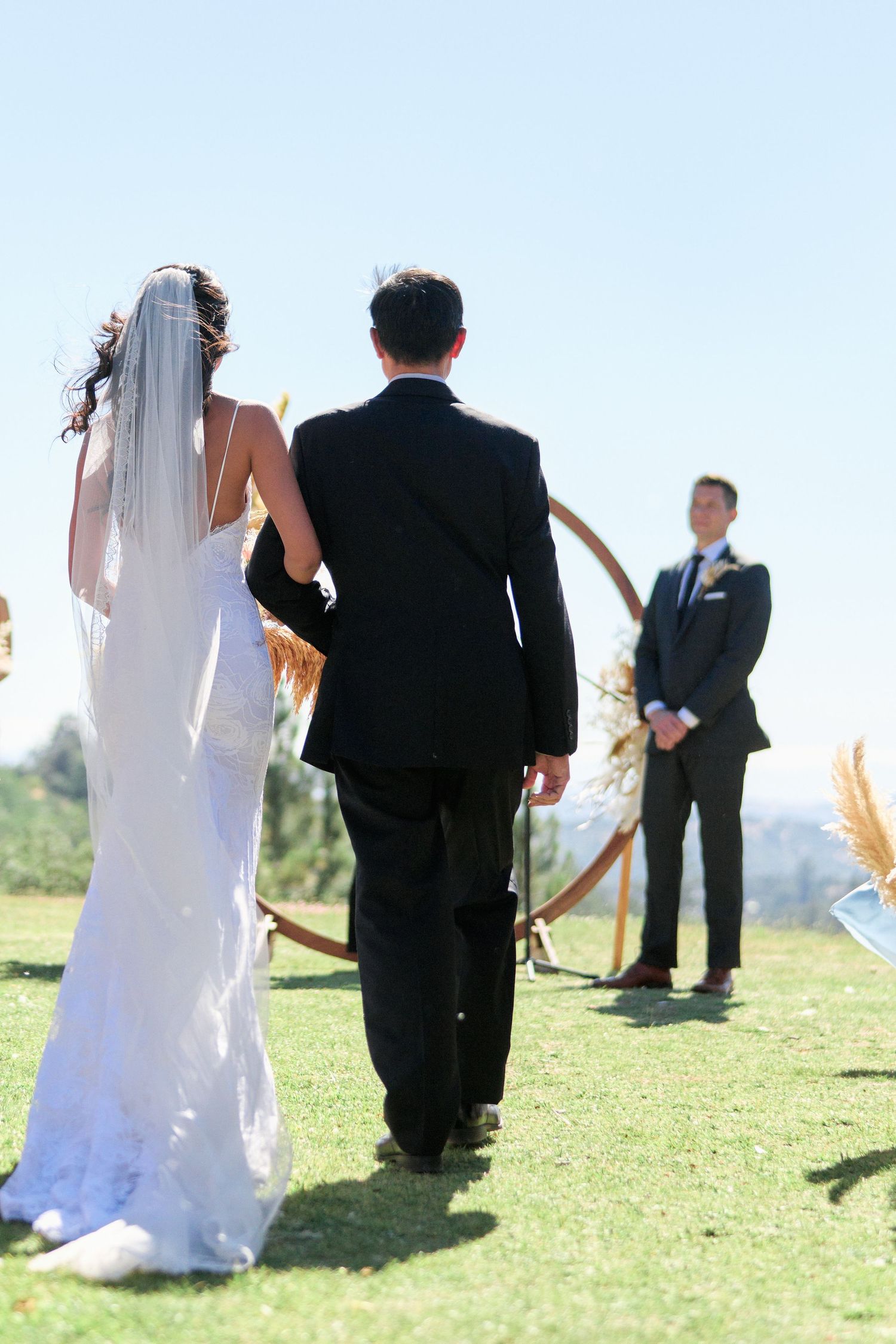 Wedding ceremony setup on a grassy hilltop with an arch and officiant under blue skies.